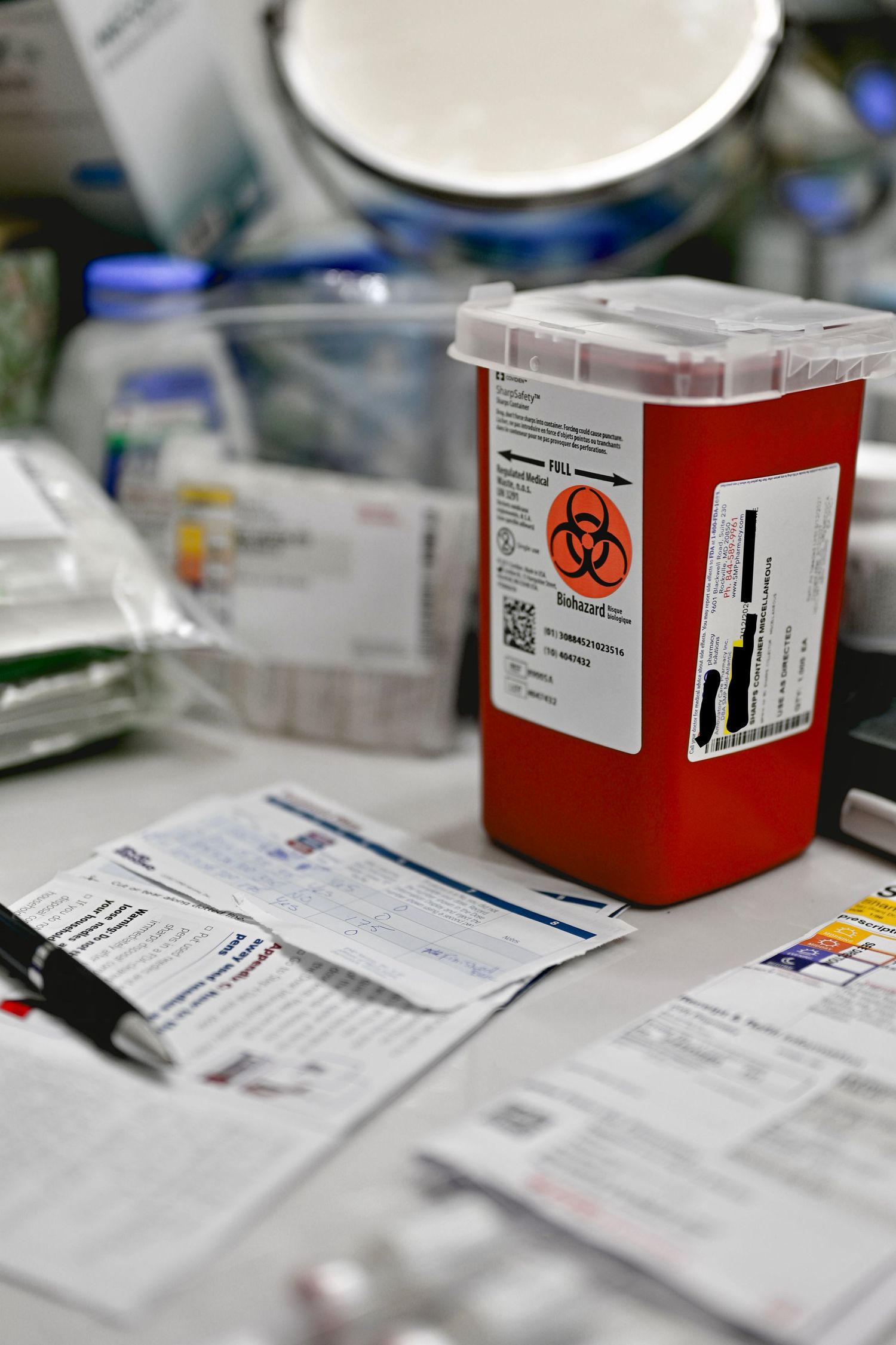 Medical biohazard container and paperwork on desk with patient forms and documentation in clinical setting.