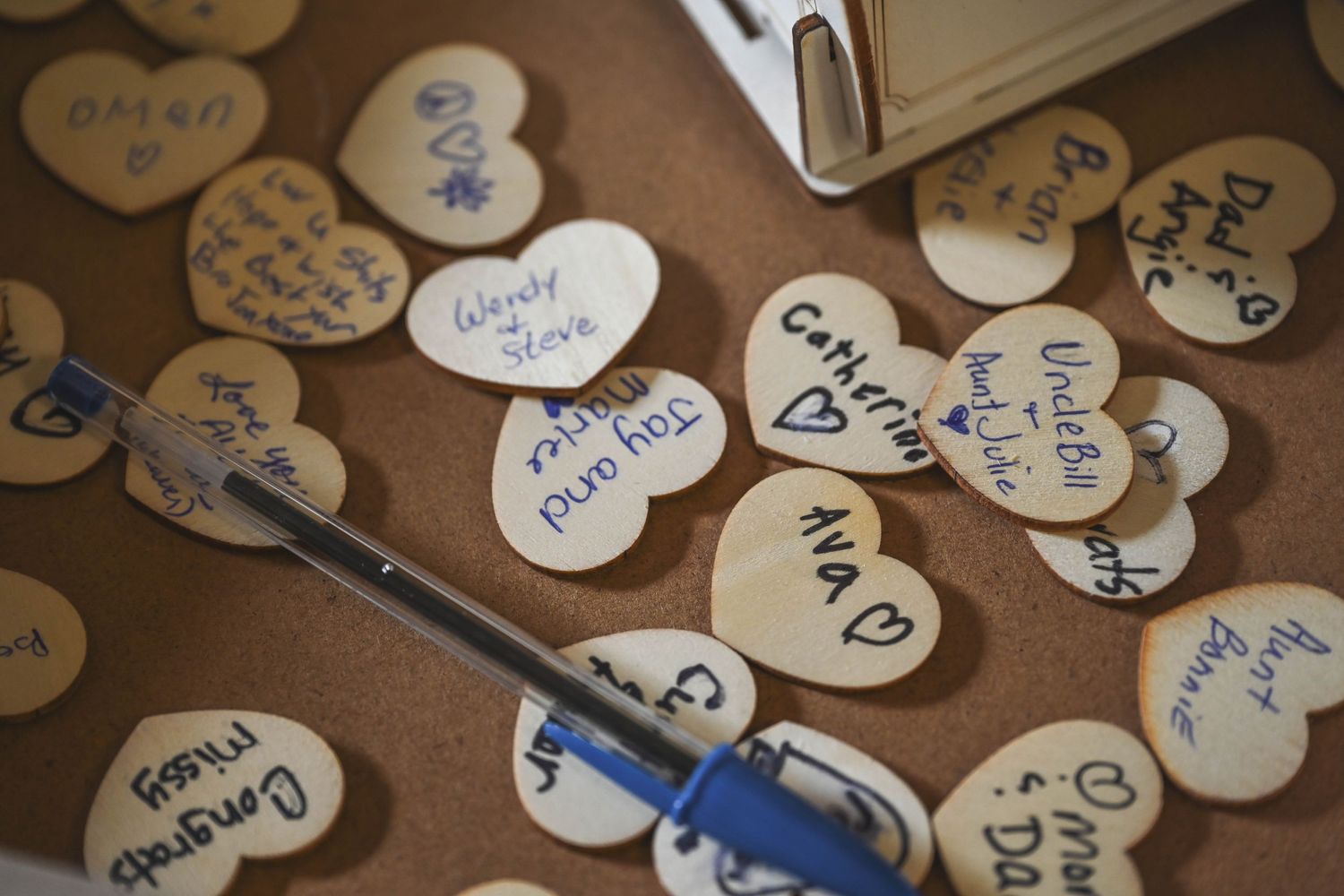 Small heart-shaped notes and messages scattered on a brown surface with a blue pen.