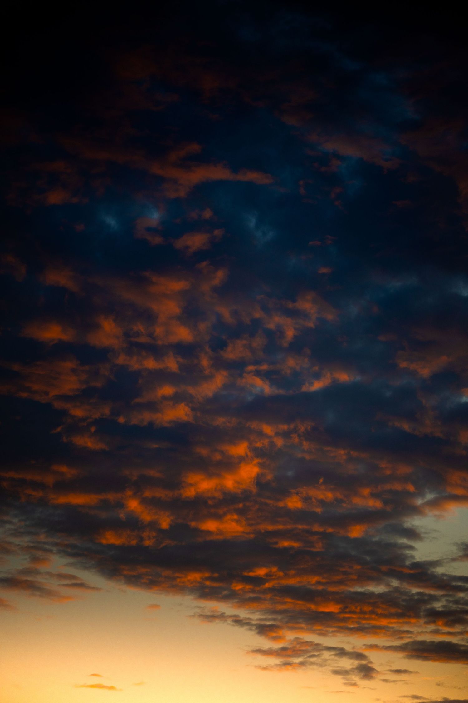 Dramatic sunset sky with deep blue clouds illuminated by vivid orange and golden light at dusk.
