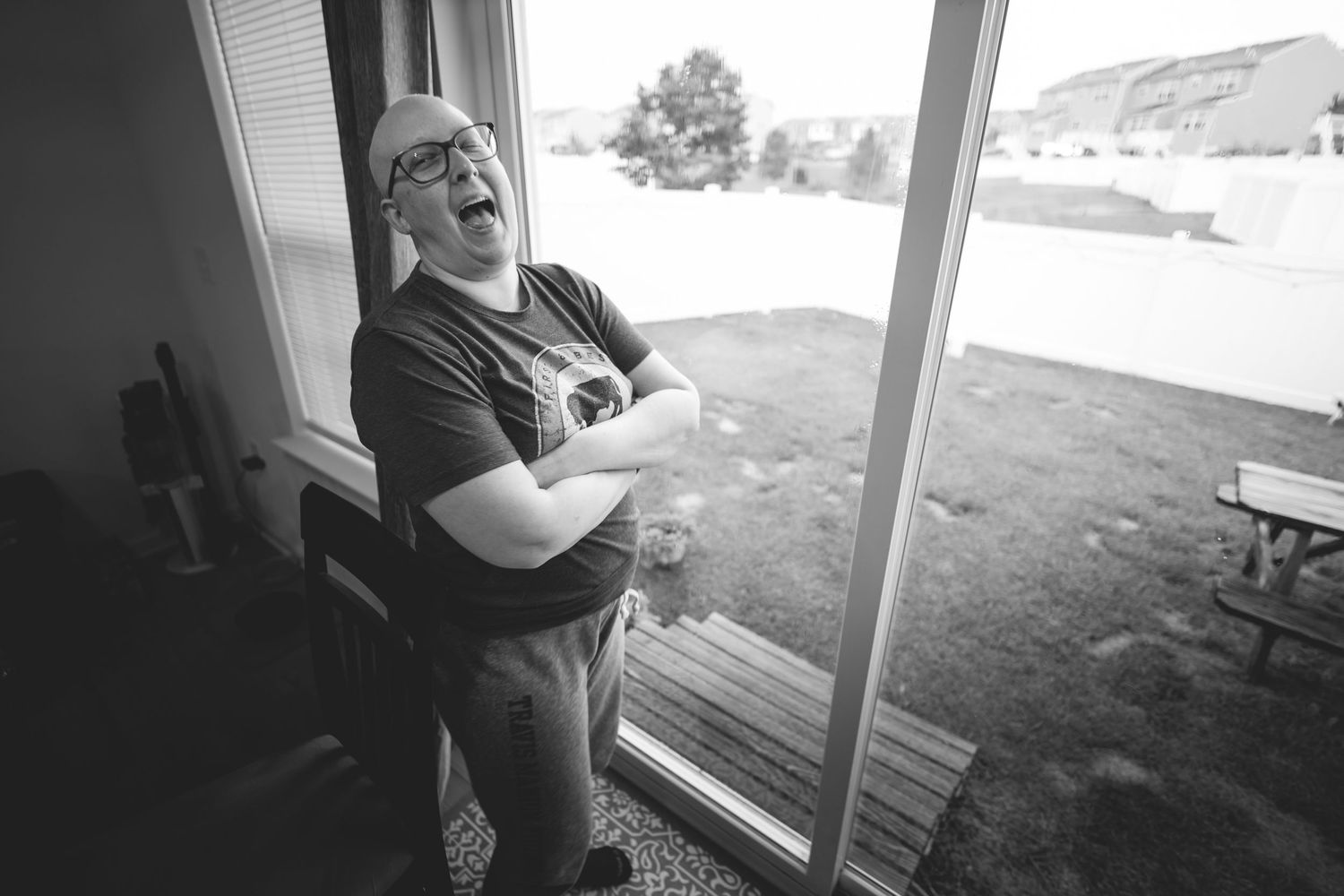 Man laughing joyfully by sliding glass door in black and white photo with outdoor landscape view.