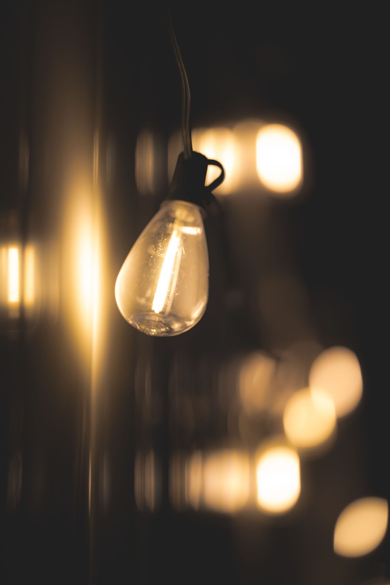 Vintage Edison filament bulb glowing warmly in the dark, with soft bokeh lights in the background.