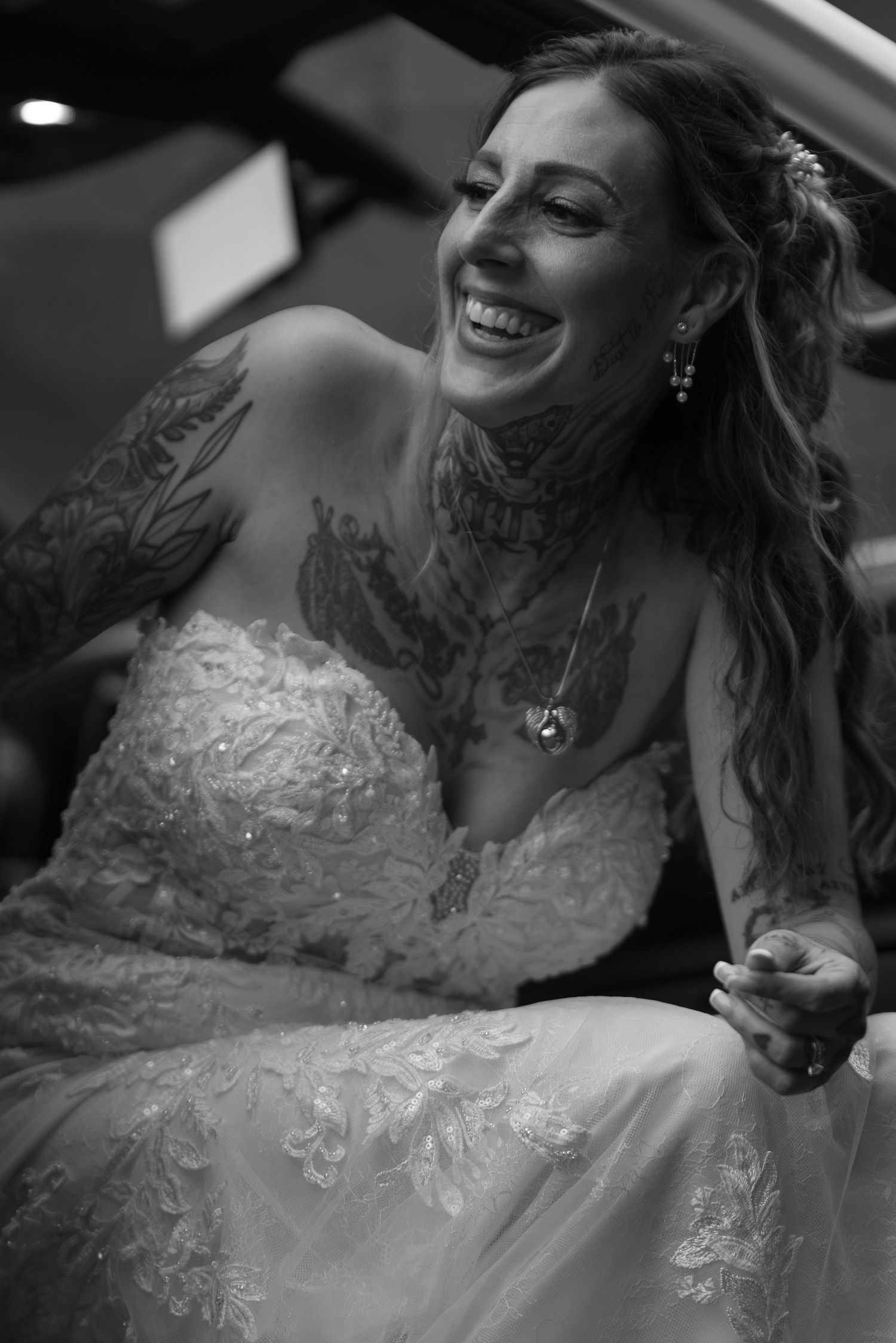 Black and white photo of a smiling tattooed bride in a strapless lace wedding gown