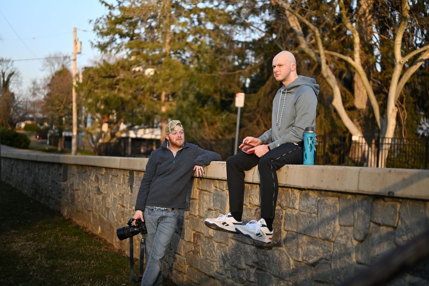 Two people having a conversation while sitting on a stone wall at sunset.
