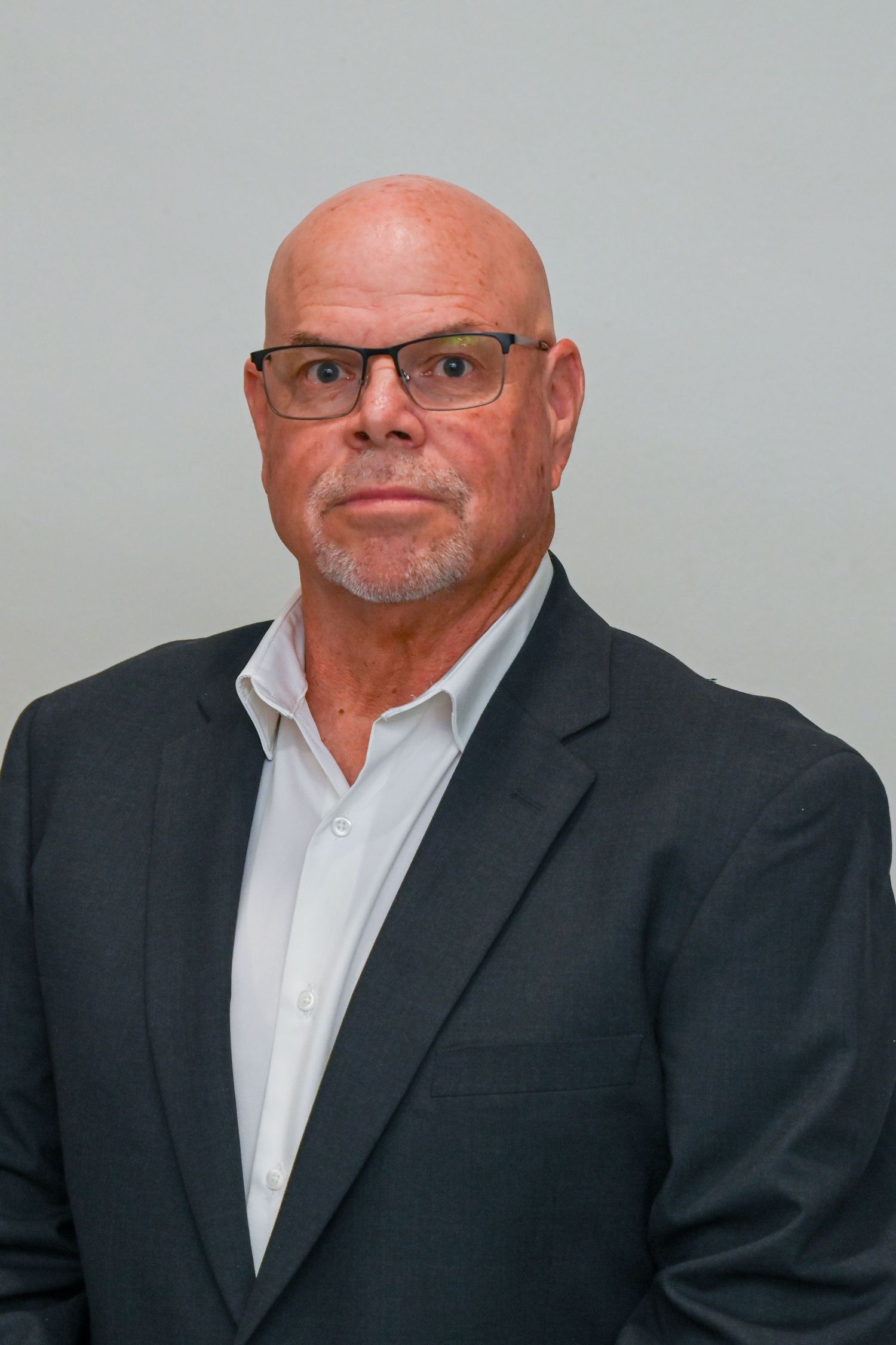 Professional headshot of a man in business attire against grey background.
