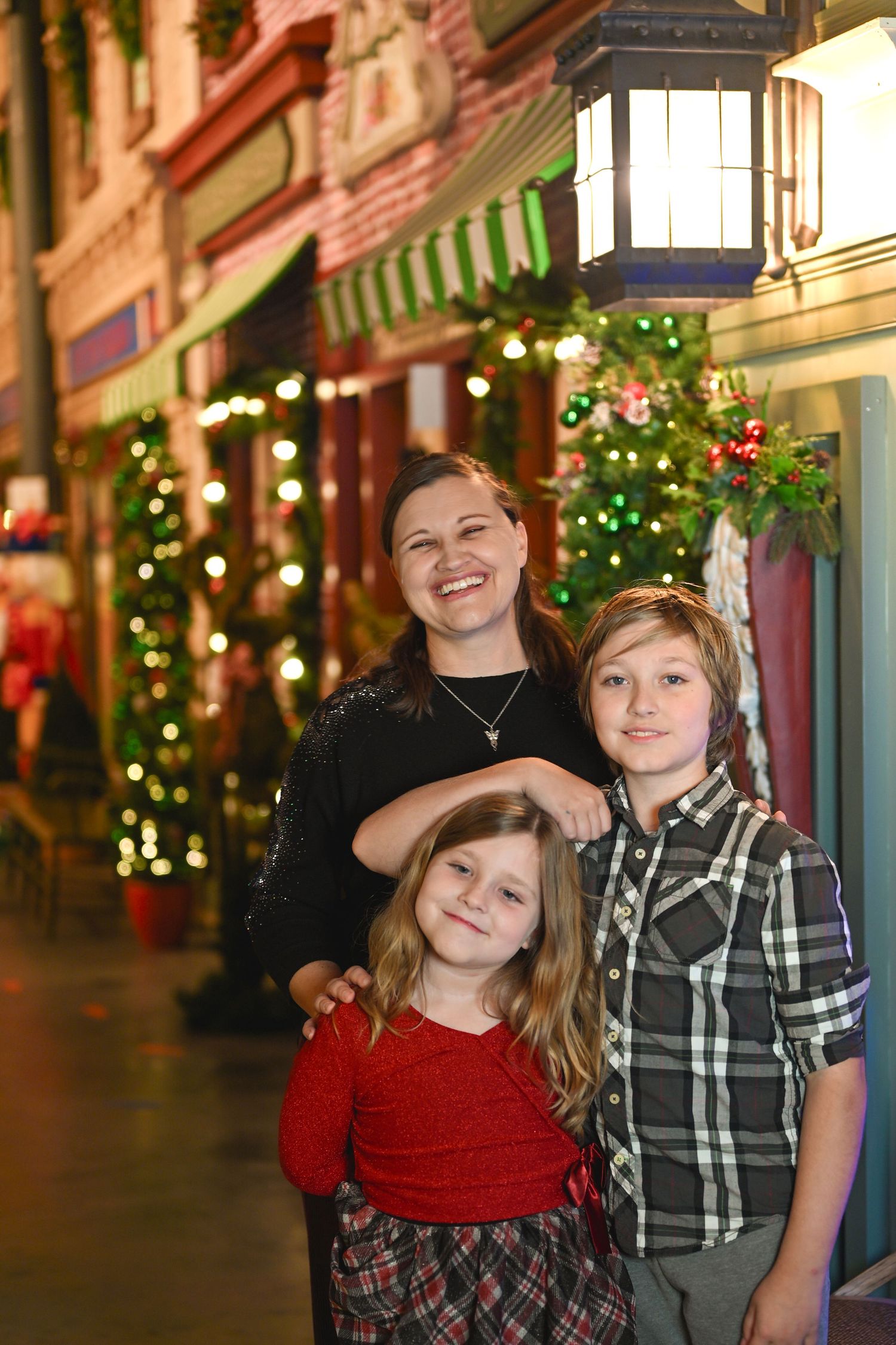 Two people pose together in front of festive holiday decorations and twinkling lights along a shopping street.