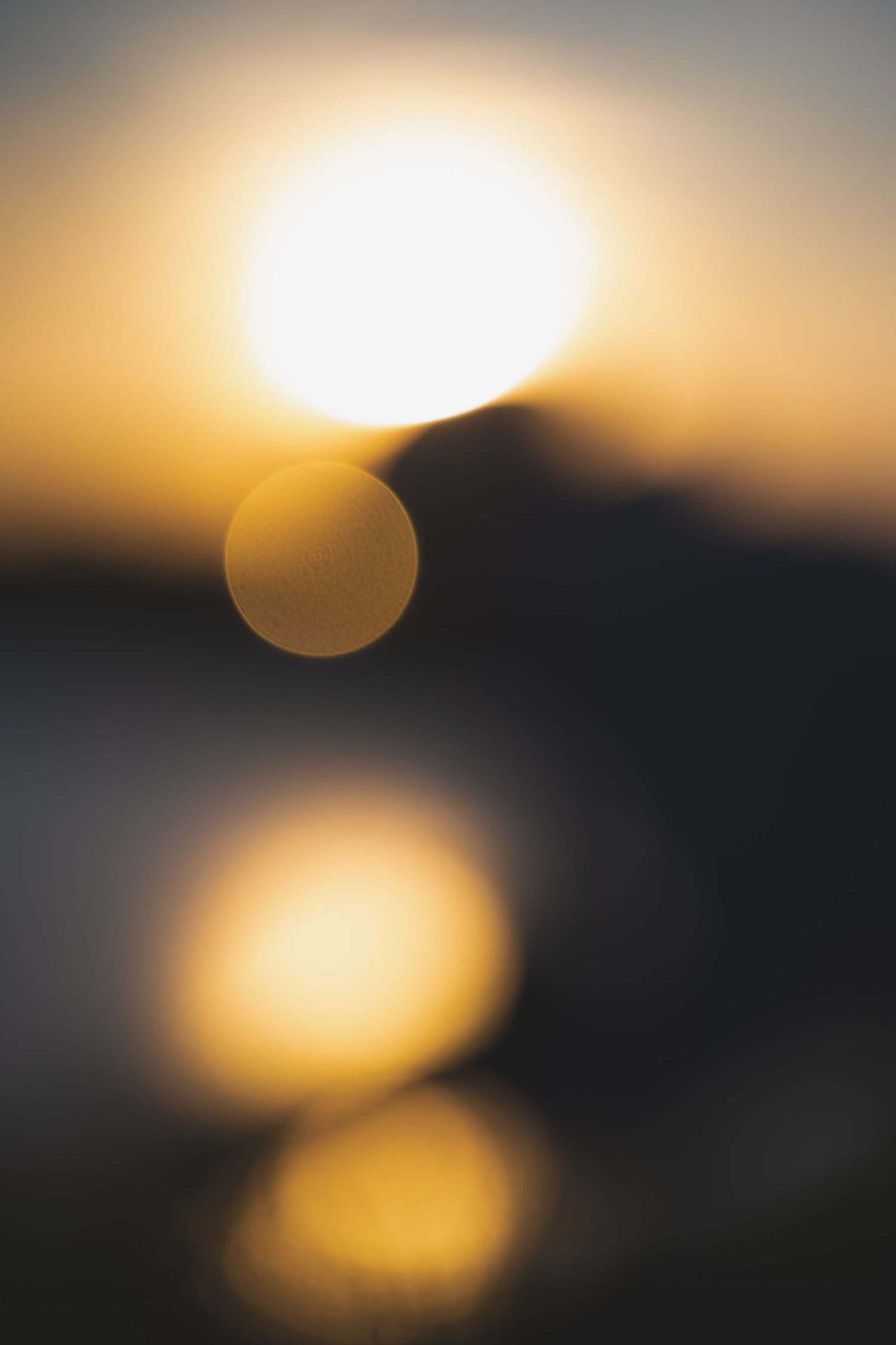 Blurred bokeh sunset with golden light orbs reflecting over dark water at dusk.