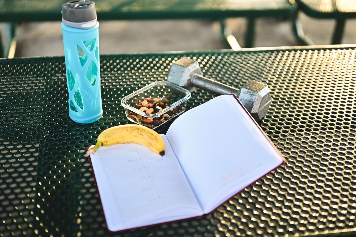 Open blank notebook on metal table with water bottle and healthy snacks for outdoor study session.