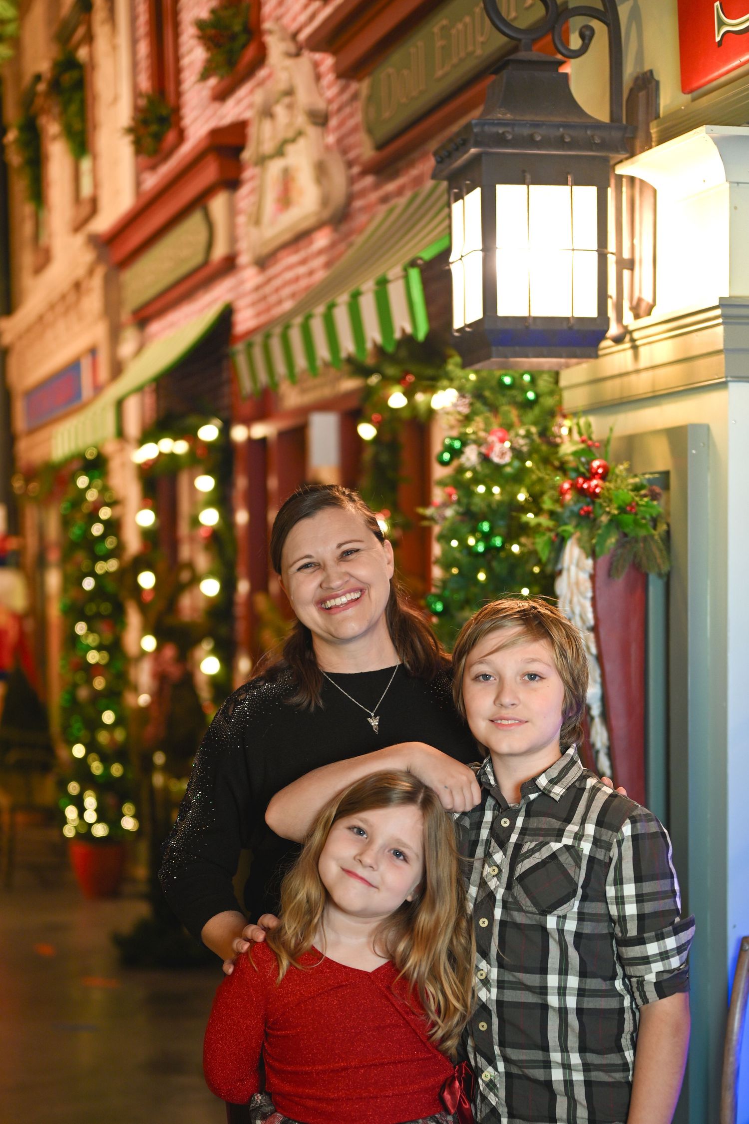 Group poses together in front of festive holiday decorations and storefronts with twinkling lights at night.