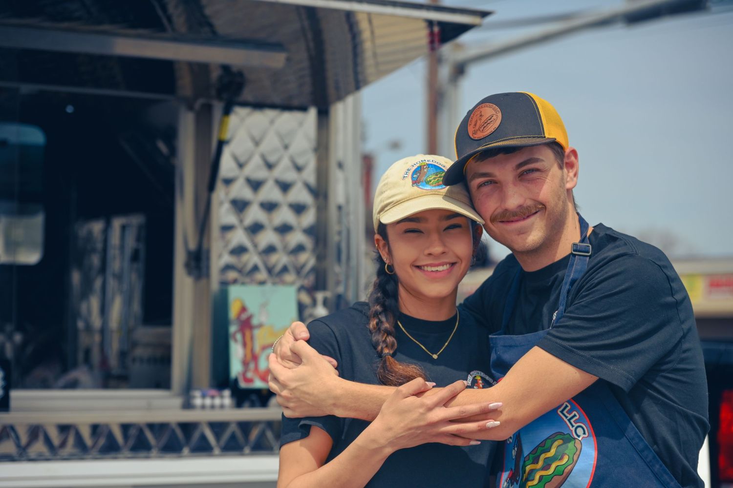 Two people smile together while sharing a moment outside a food truck with patterned geometric wall art.