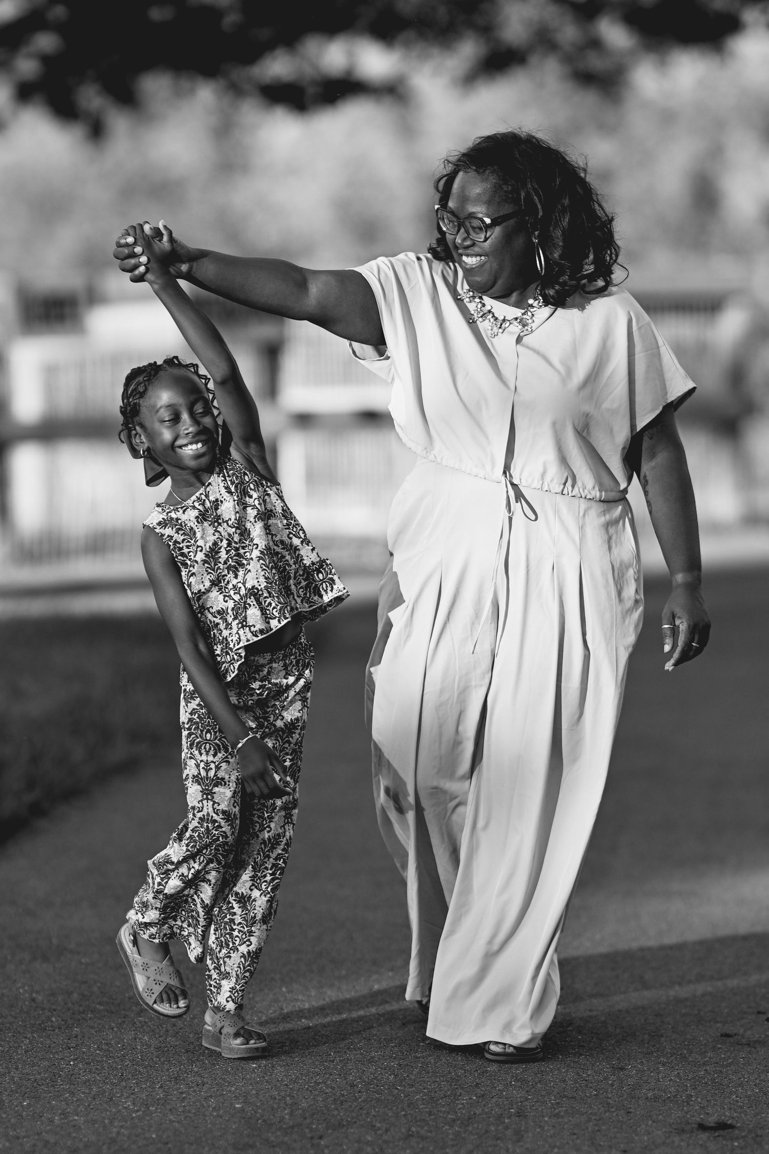Black and white photo of a woman and young girl dancing together outdoors, holding hands and smiling joyfully.