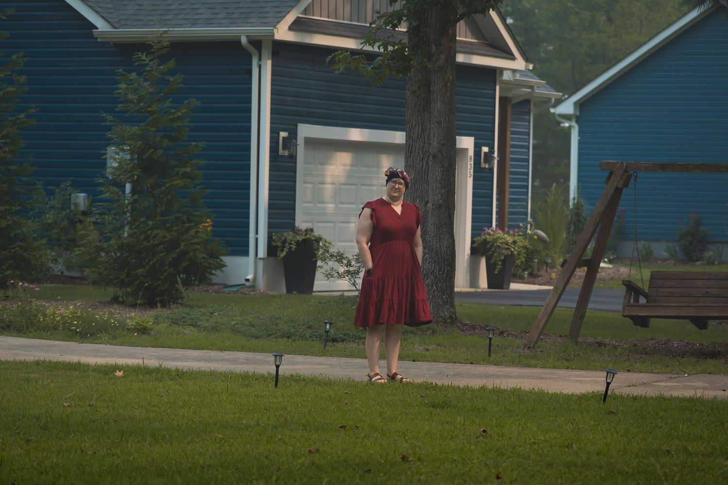 Woman in red dress standing on green lawn in front of blue house with swing set.