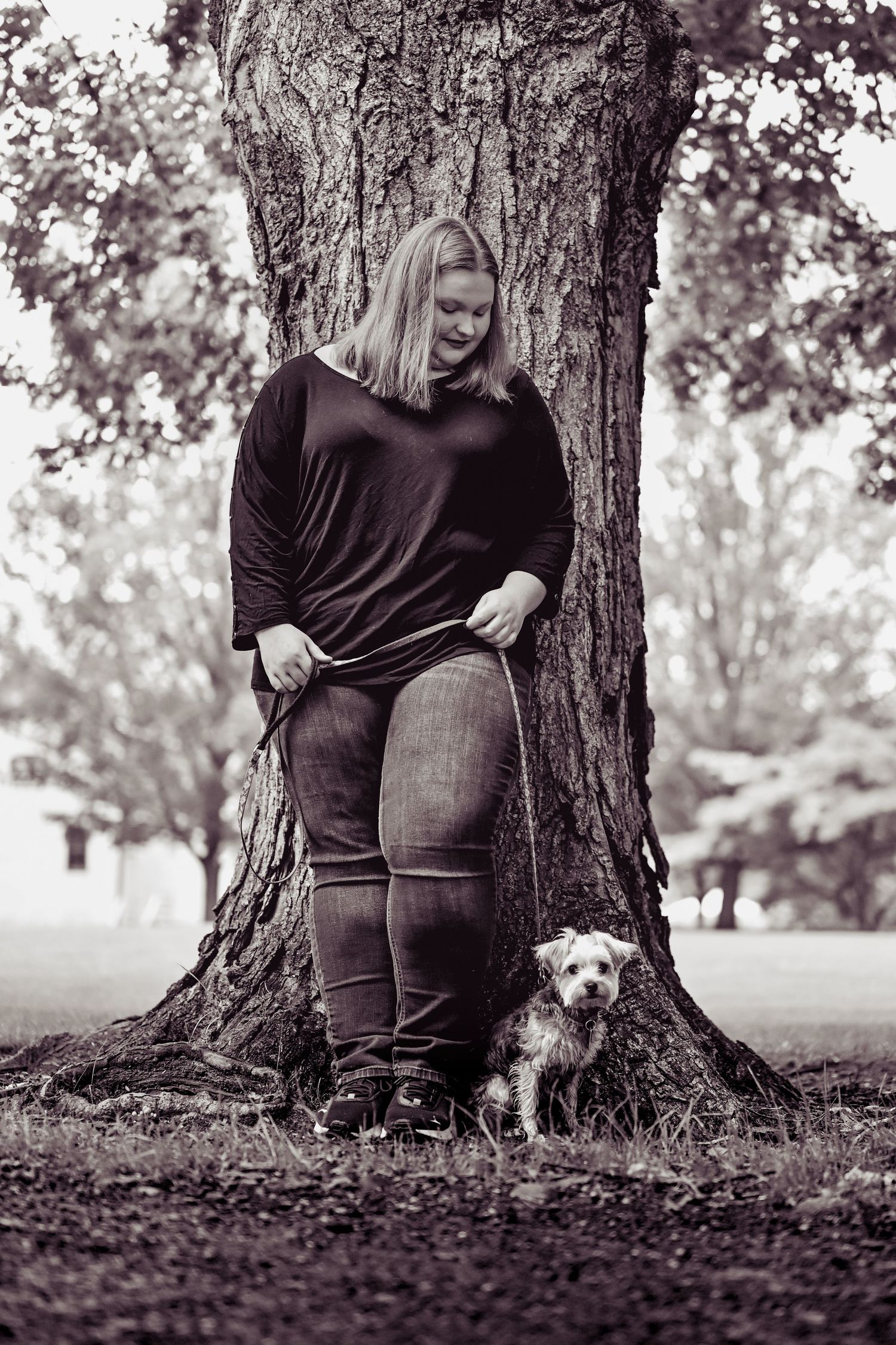 Four black and white artistic photos show a person sitting by a tree trunk with a small dog in nature.