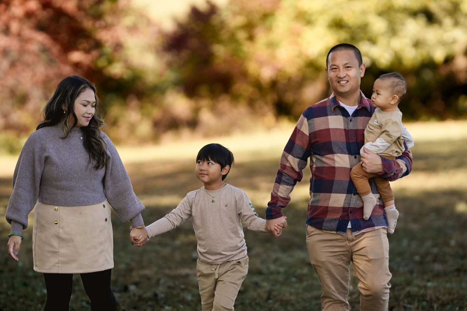 A family walks together holding hands on an autumn day in a park with golden sunlight in the background.