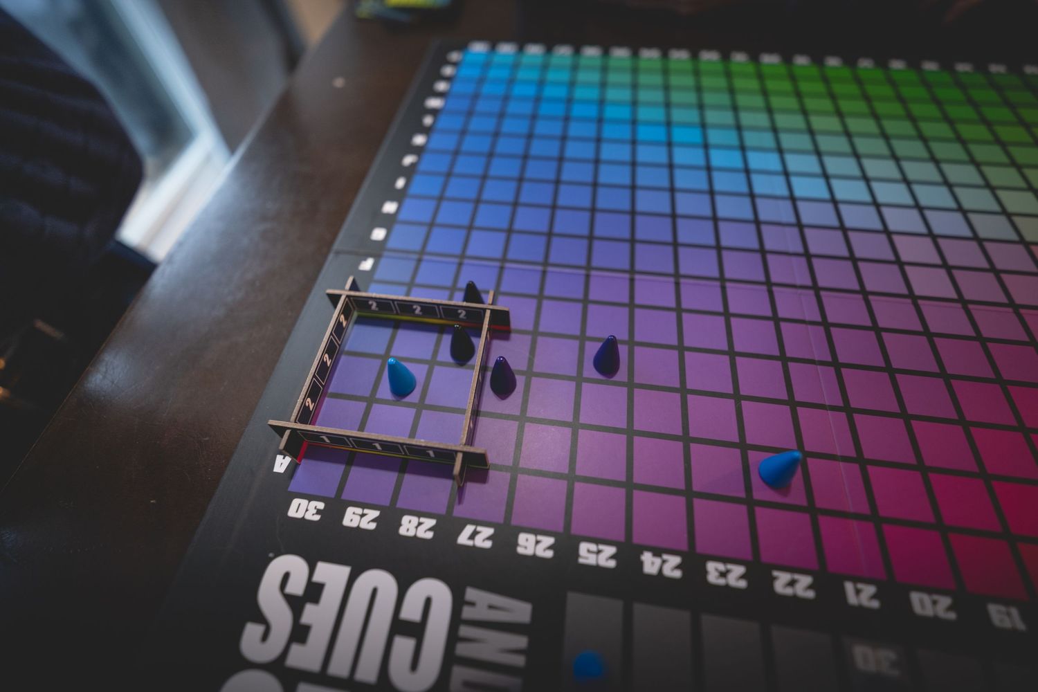 Colorful rainbow grid board game called Cues with game pieces placed on vibrant gradient squares.