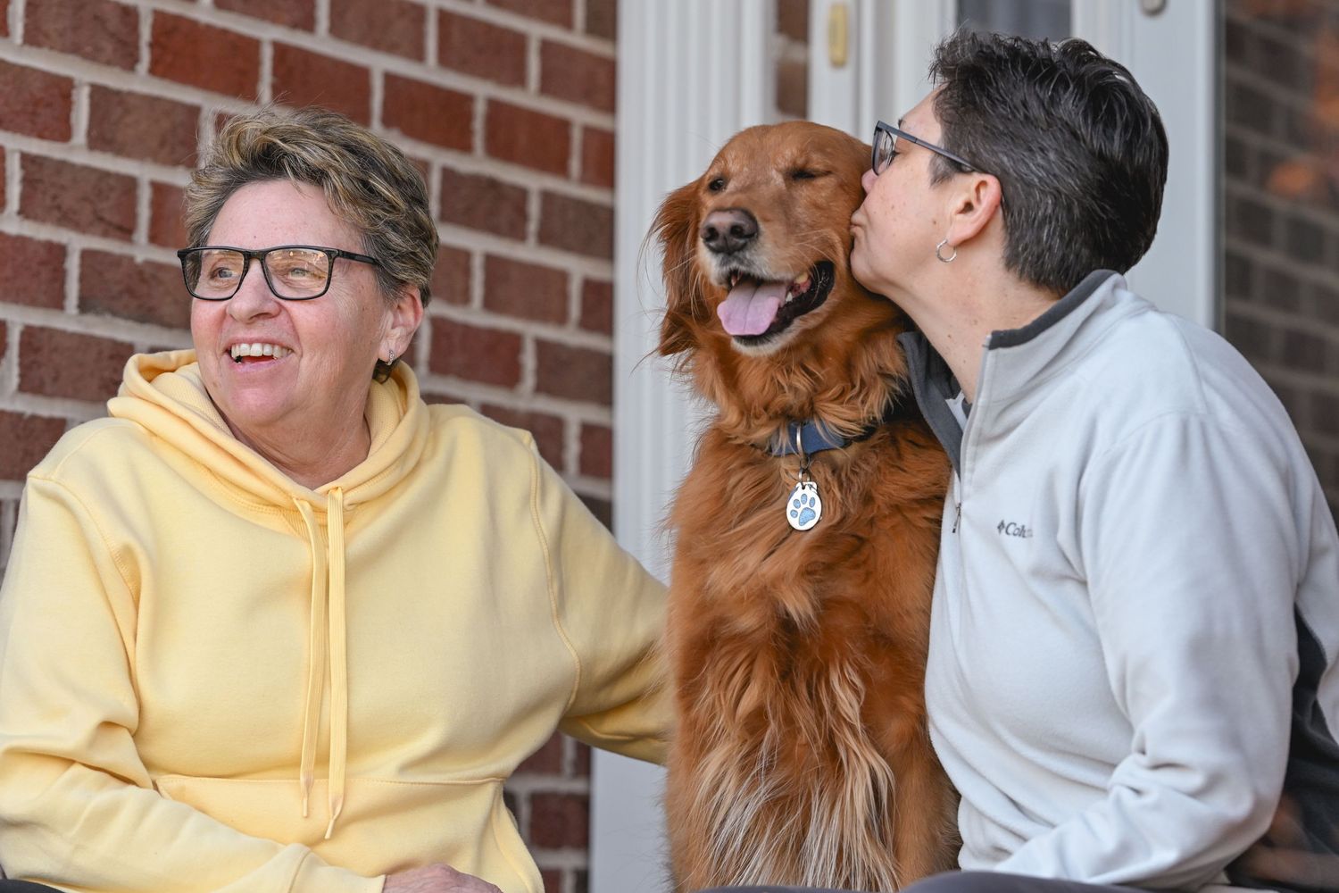 Two people sharing a joyful moment with their golden retriever on a porch.