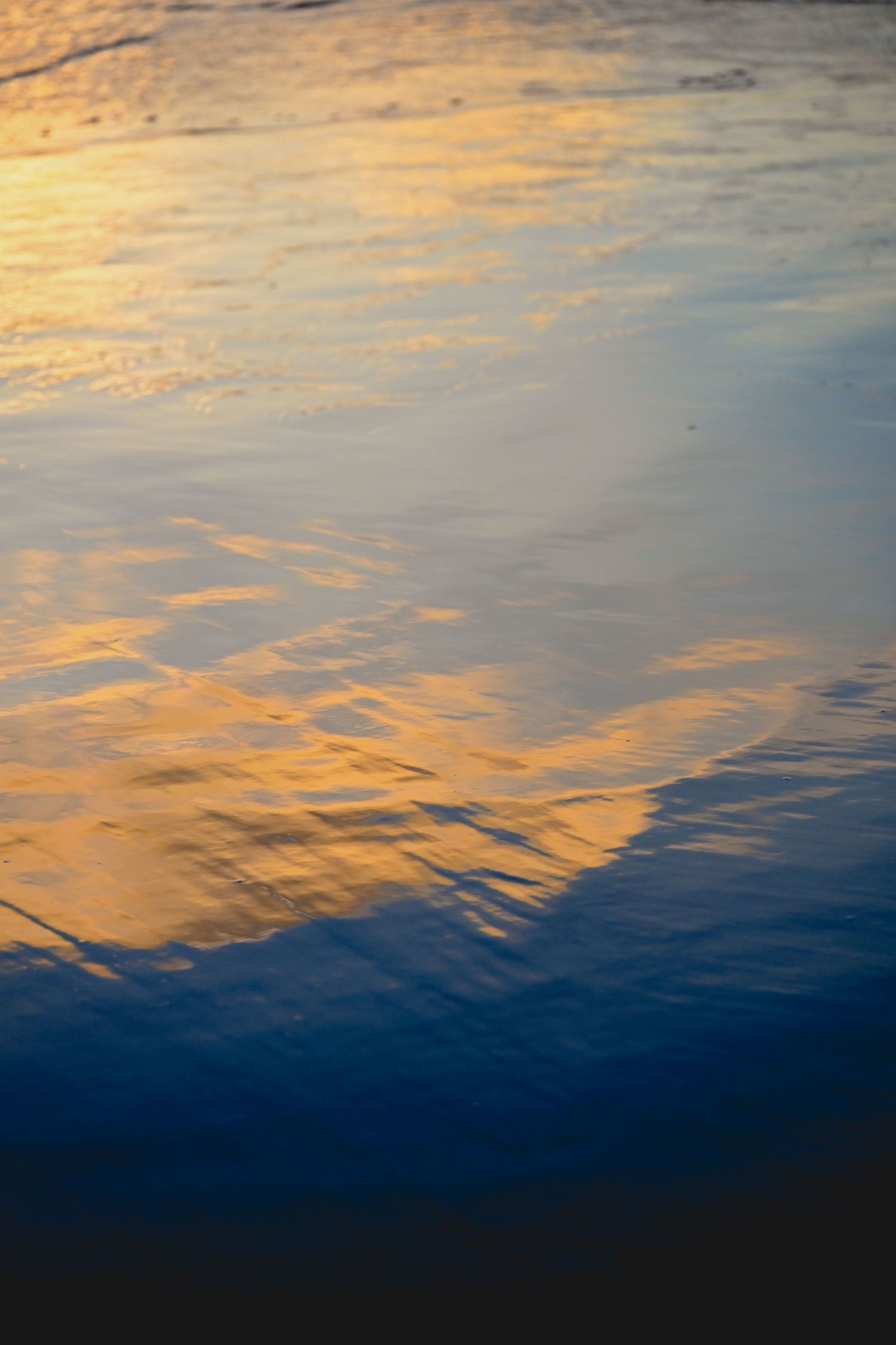 Golden sunset light reflecting on calm rippling water surface with blue and orange hues.