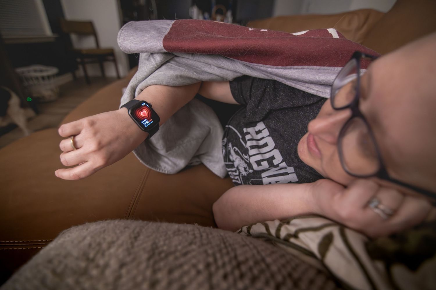 Person resting on a couch wearing glasses and a smartwatch with a Dominos logo, shirt pulled over their head.