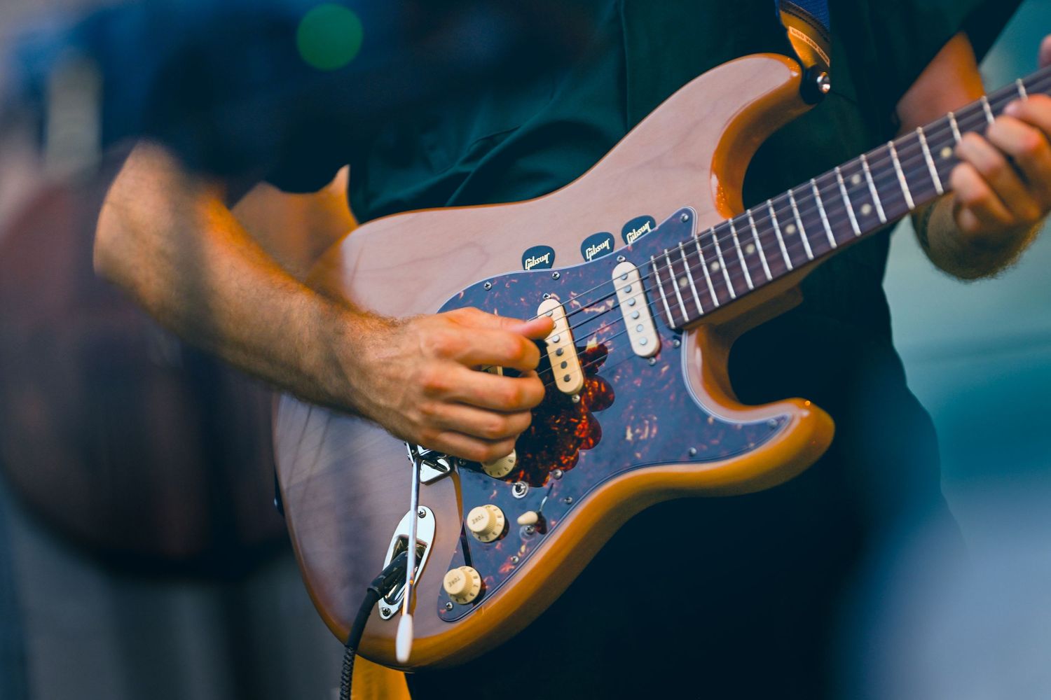 Close-up shot of hands playing an electric guitar with blue lighting and bokeh effects in the background.
