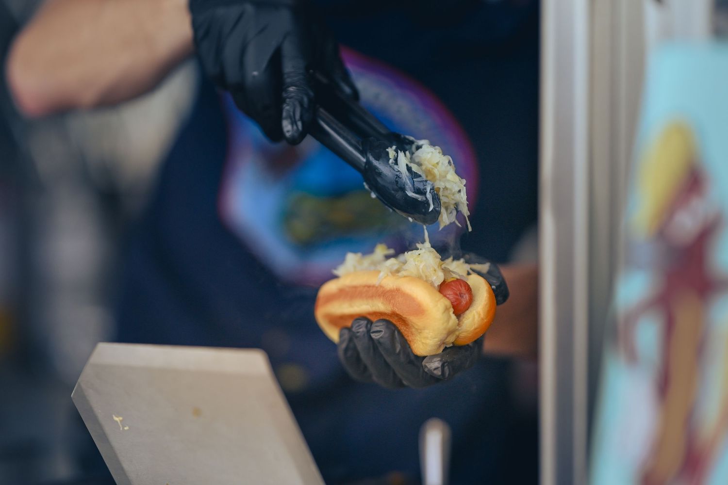 Chef using black tongs to garnish a hot dog.