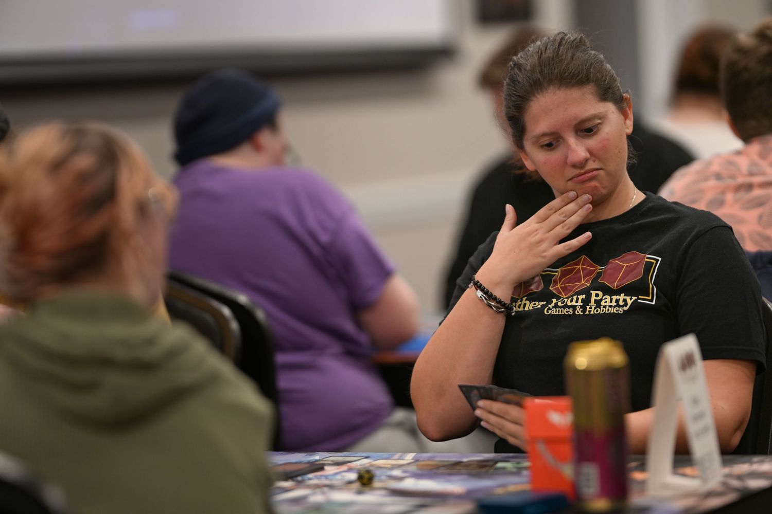 A person in a black t-shirt sits at a table pondering their next move during what appears to be a game session.