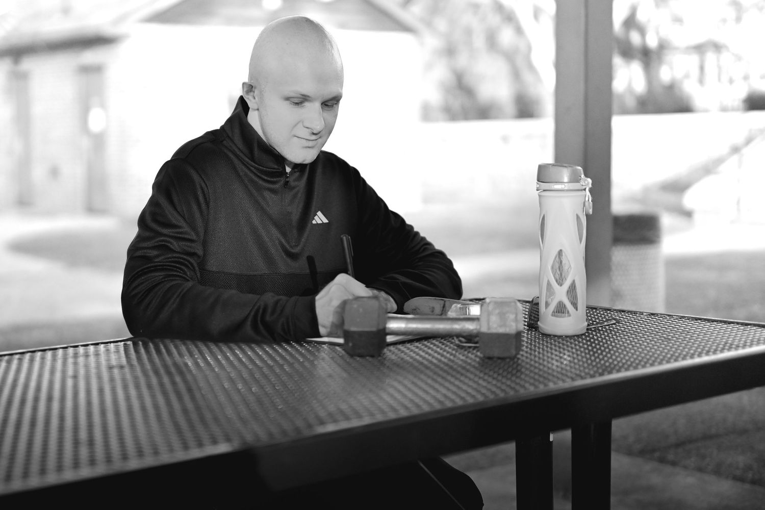 Person sitting alone at an outdoor metal table with a drink in black and white photography.