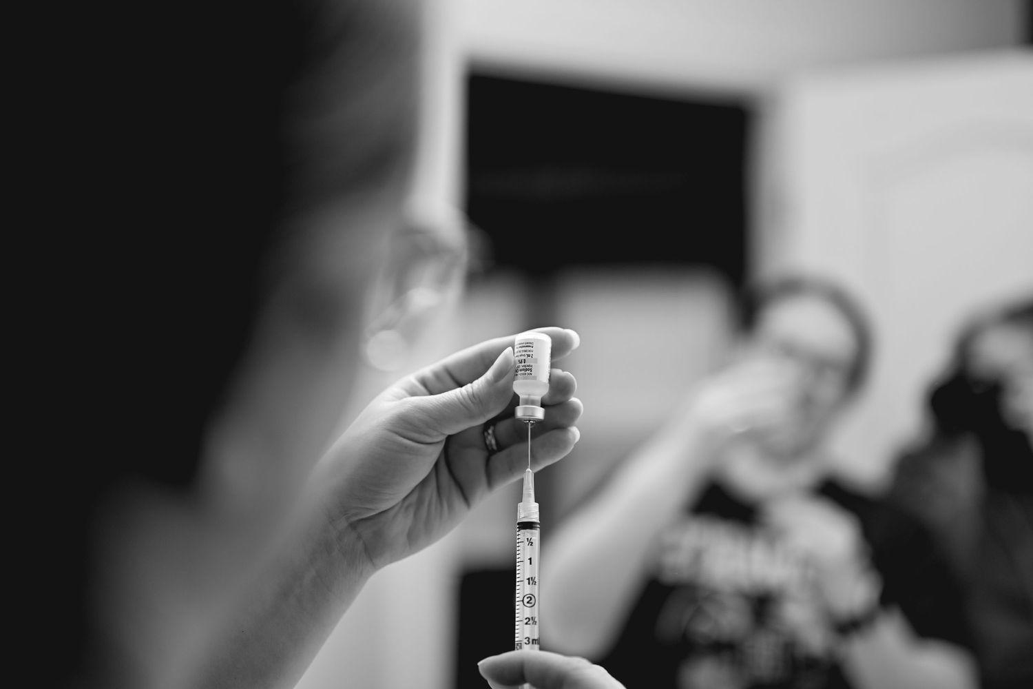 Hands holding up small vials containing clear liquid samples against a blurred background.