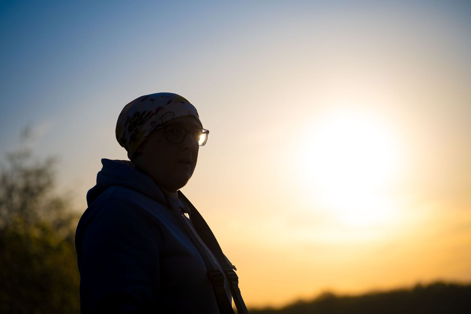 Silhouette of a person wearing glasses and a cap against a warm golden sunset sky.