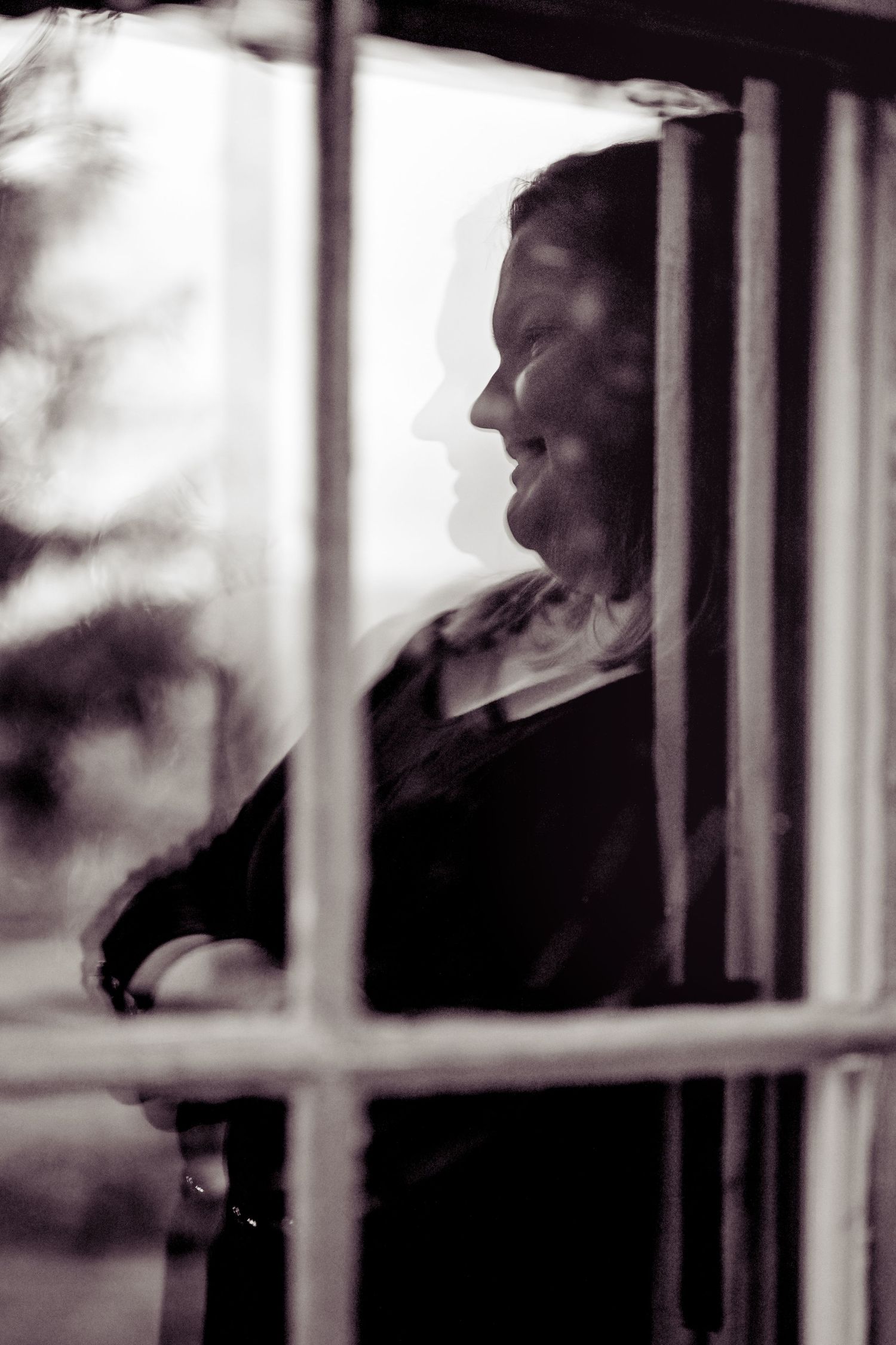 Silhouetted figures appear through window panes in a moody black and white photograph.