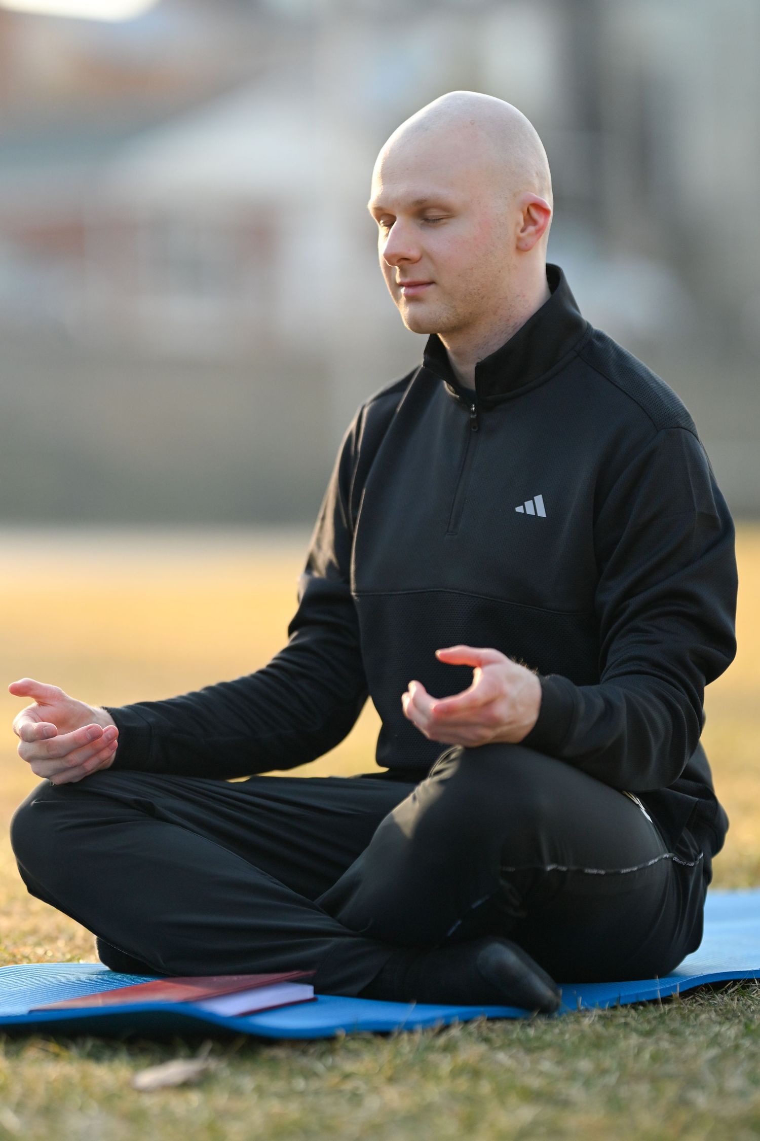 Person in black athletic wear meditating on yoga mat outdoors.