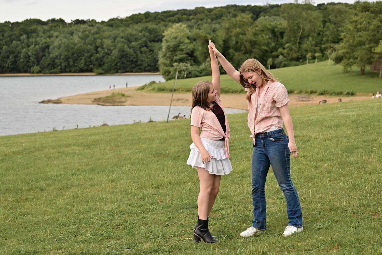 Two people share a high-five celebration while standing on grassy lakeside shore on a sunny summer day.