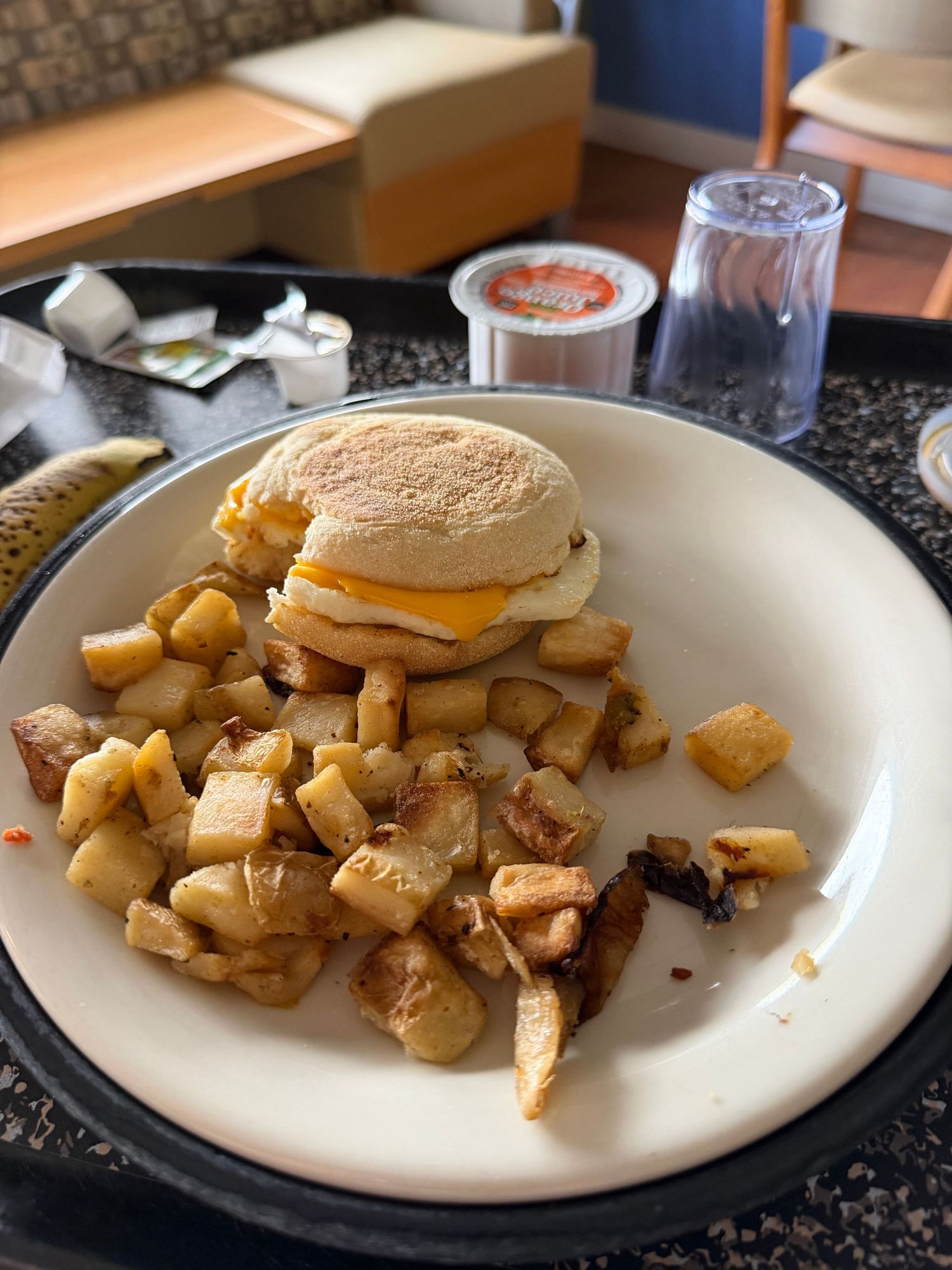 Egg and cheese sandwich on English muffin served with seasoned home fries on white plate at restaurant.