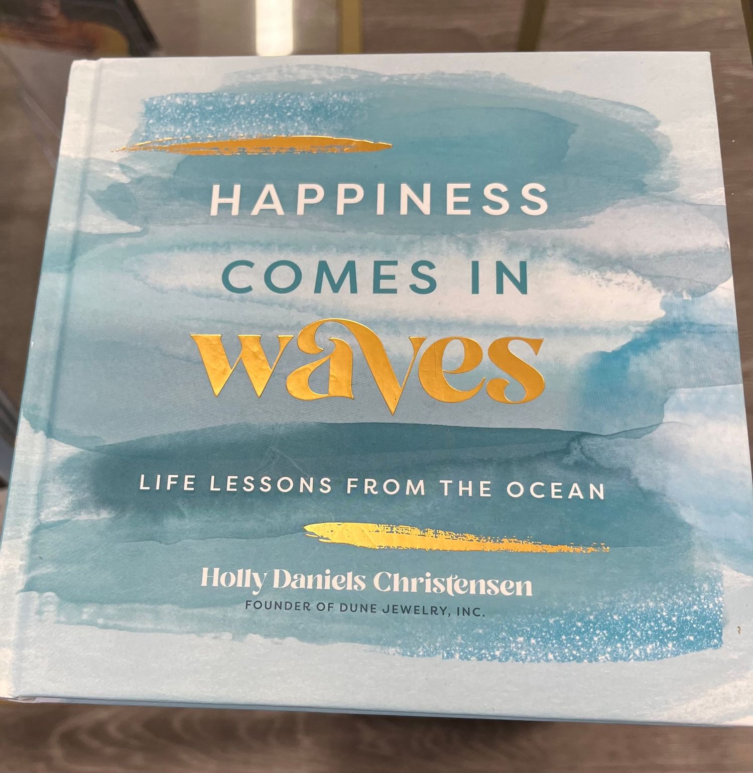 A series of blue and white book cover featuring ocean waves and the word 'Happiness comes in waves' in gold lettering.