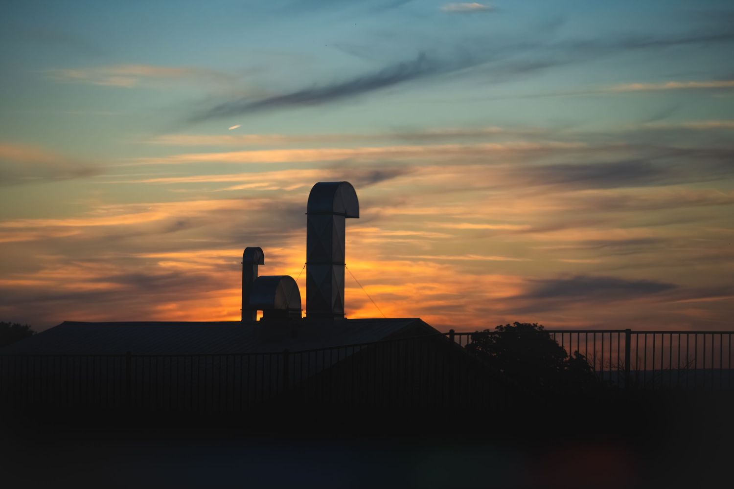 Silhouette of industrial rooftop vents against a vibrant orange and blue sunset sky.