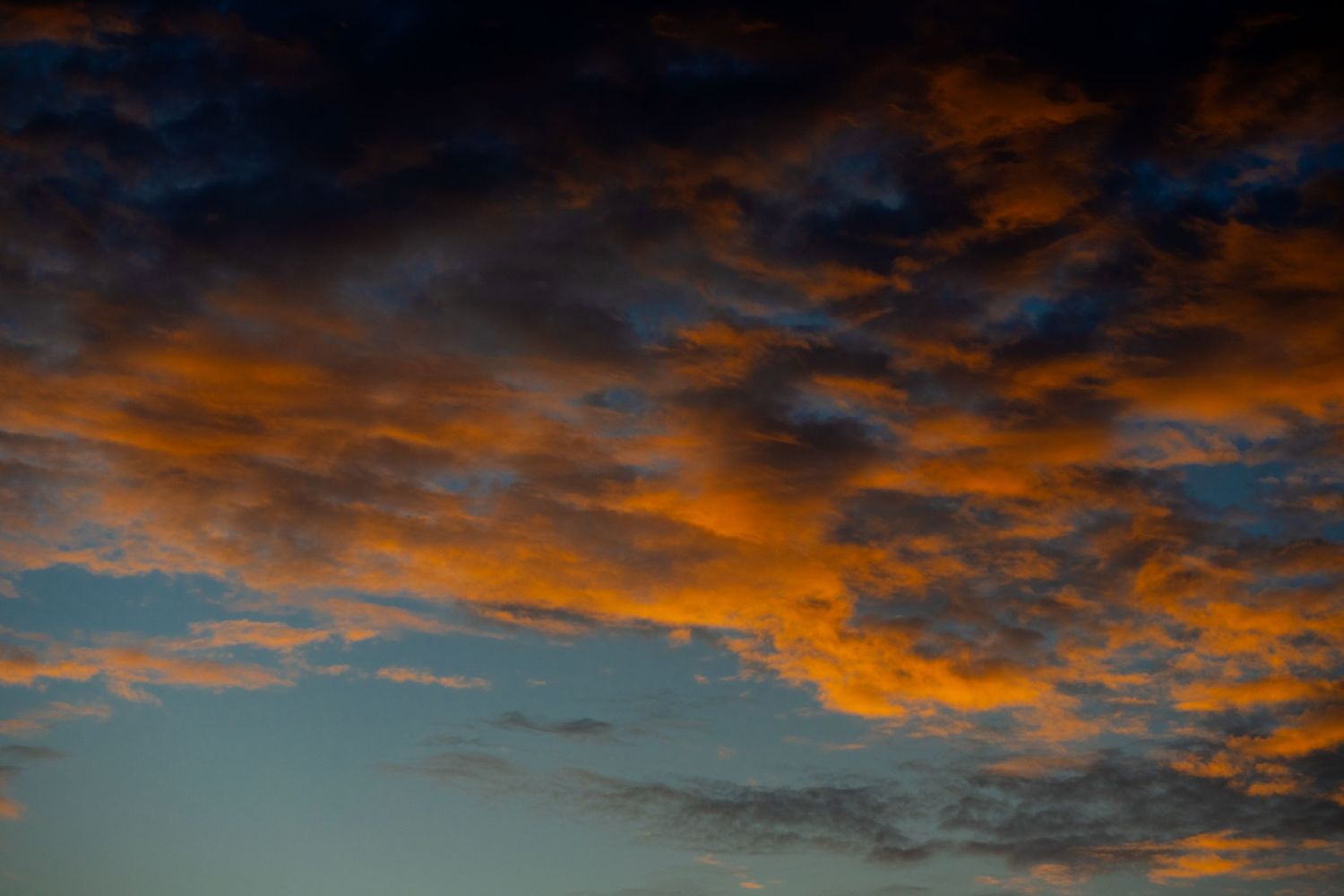 Dramatic sunset sky with vivid orange and golden clouds against deep blue twilight backdrop.