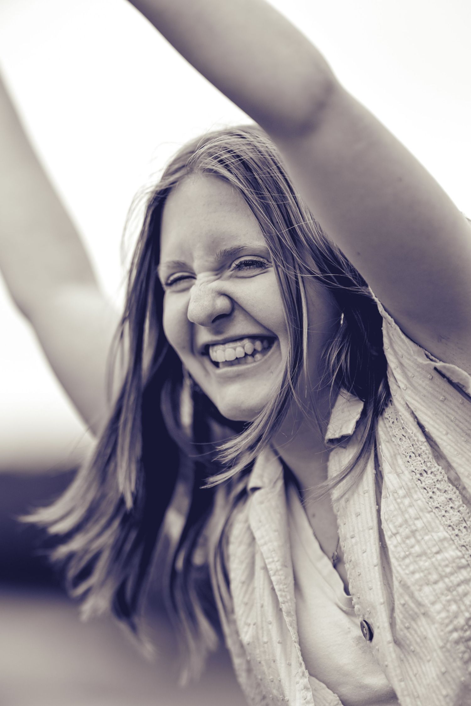 Black and white portrait of a natural, candid laugh with wind-blown hair against a blurred background.