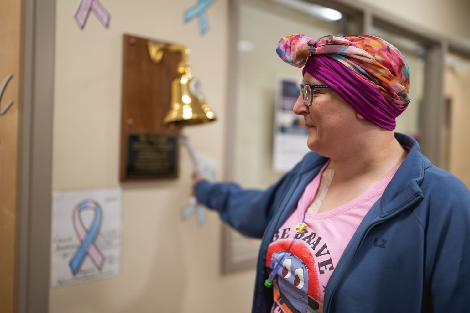 Cancer patient in colorful headscarf rings victory bell at hospital, celebrating end of cancer treatment.