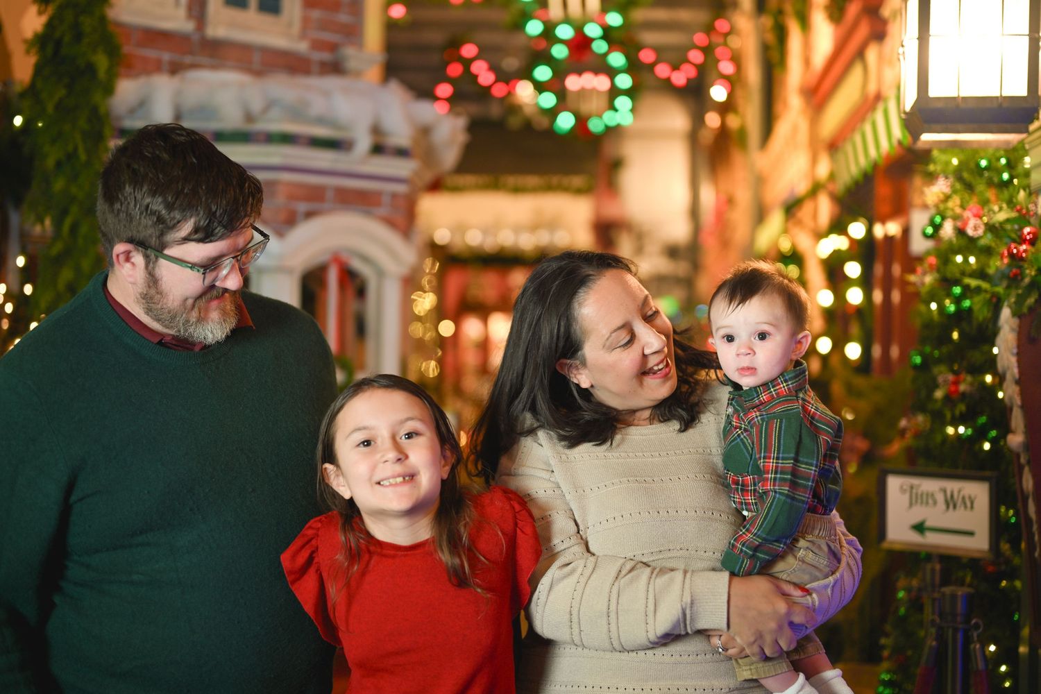 Family enjoying holiday lights and decorations at night with festive Christmas wreaths and twinkling lights in background.