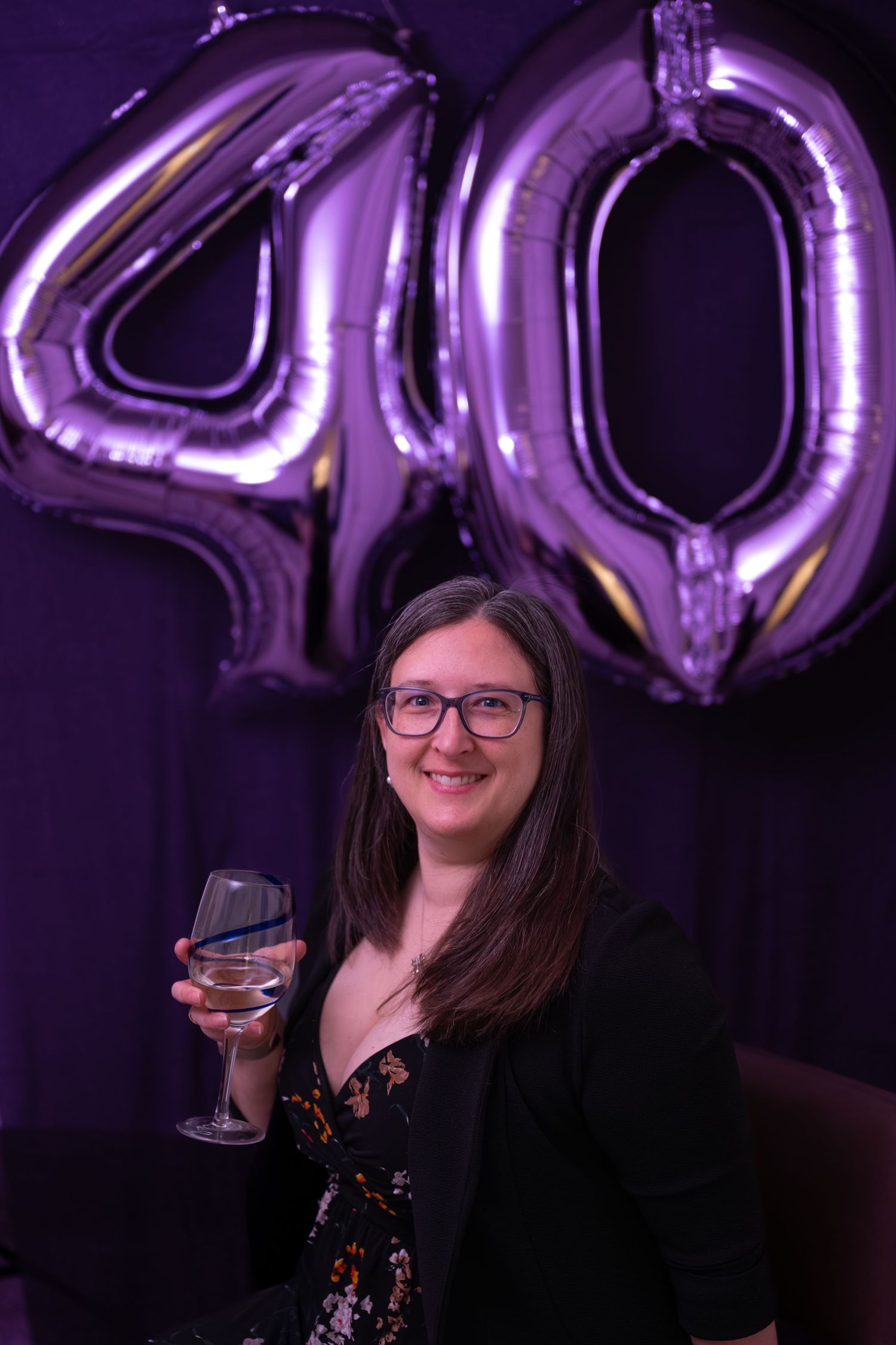 A celebratory scene with purple metallic number balloons and wine glasses against a dark background.