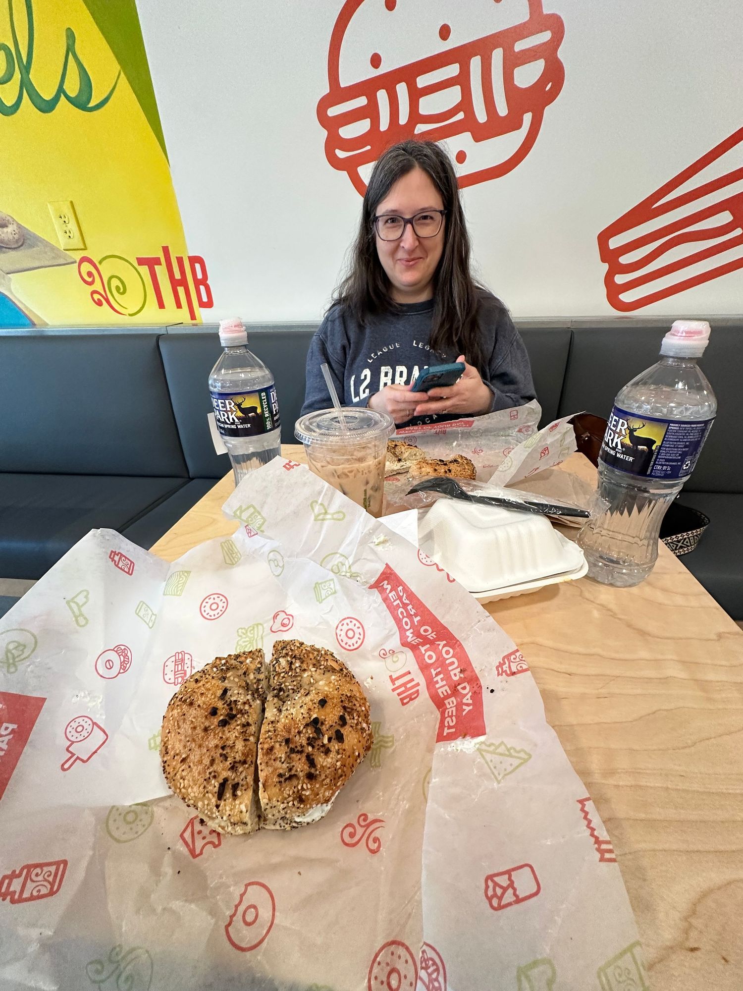 Someone sits at a casual restaurant table with a burger and drinks while surrounded by colorful wall art and branding.