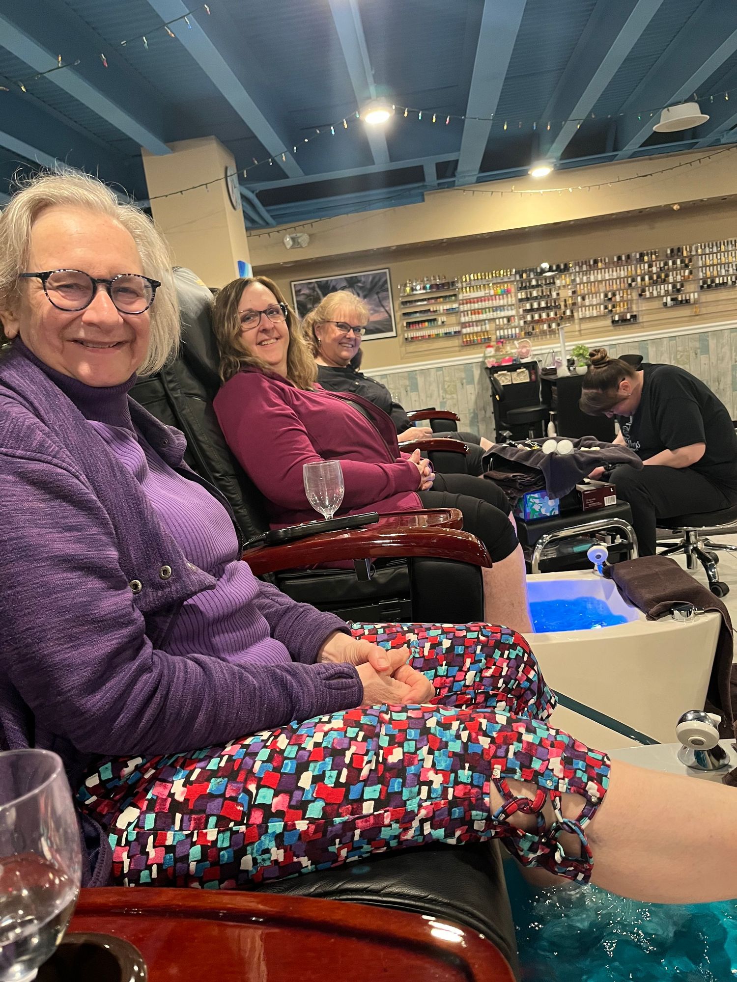 People relaxing in pedicure spa chairs wearing colorful clothing during a nail salon visit.