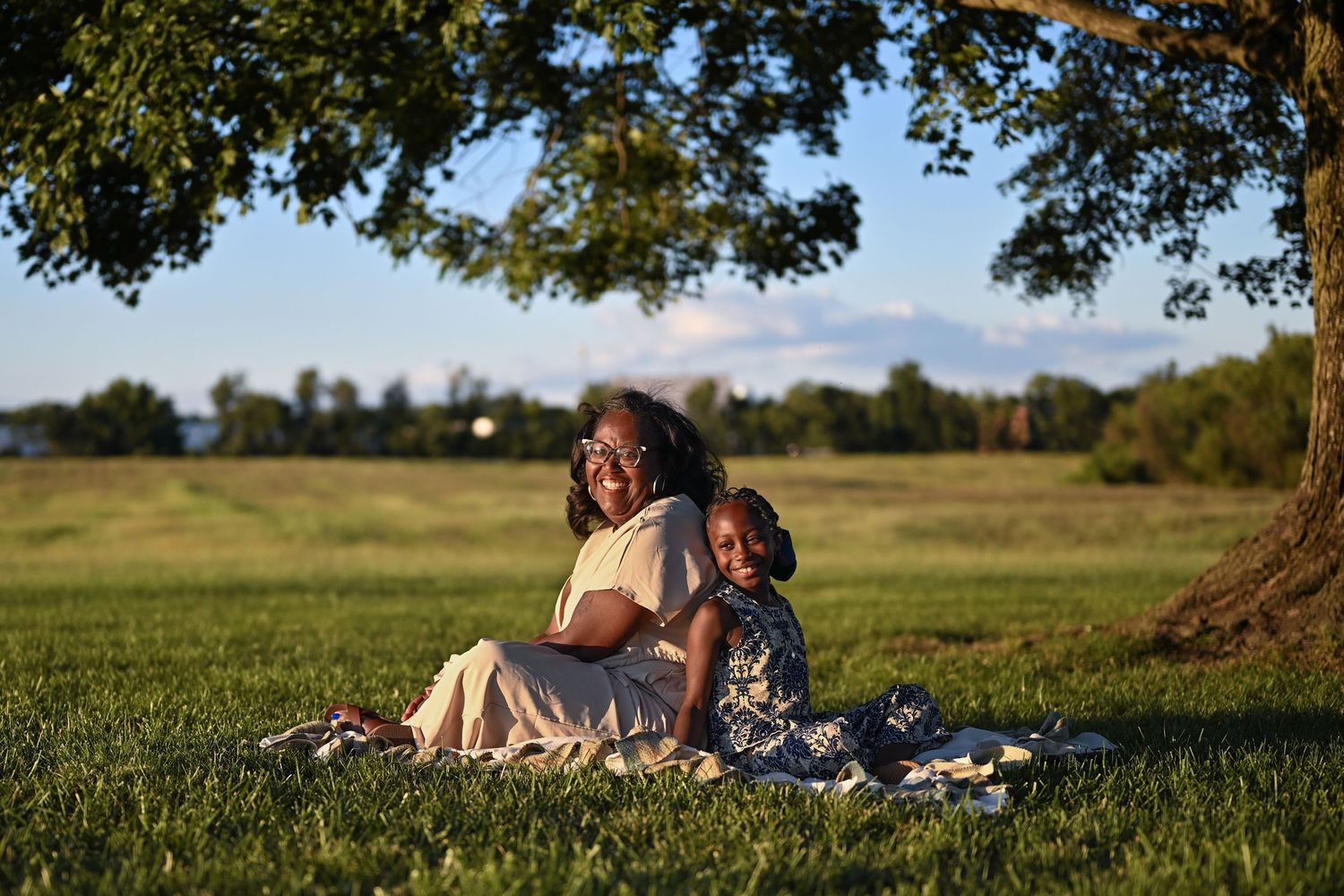 A child and mother sitting outside on a blanket in a sunny green field during a summer afternoon.