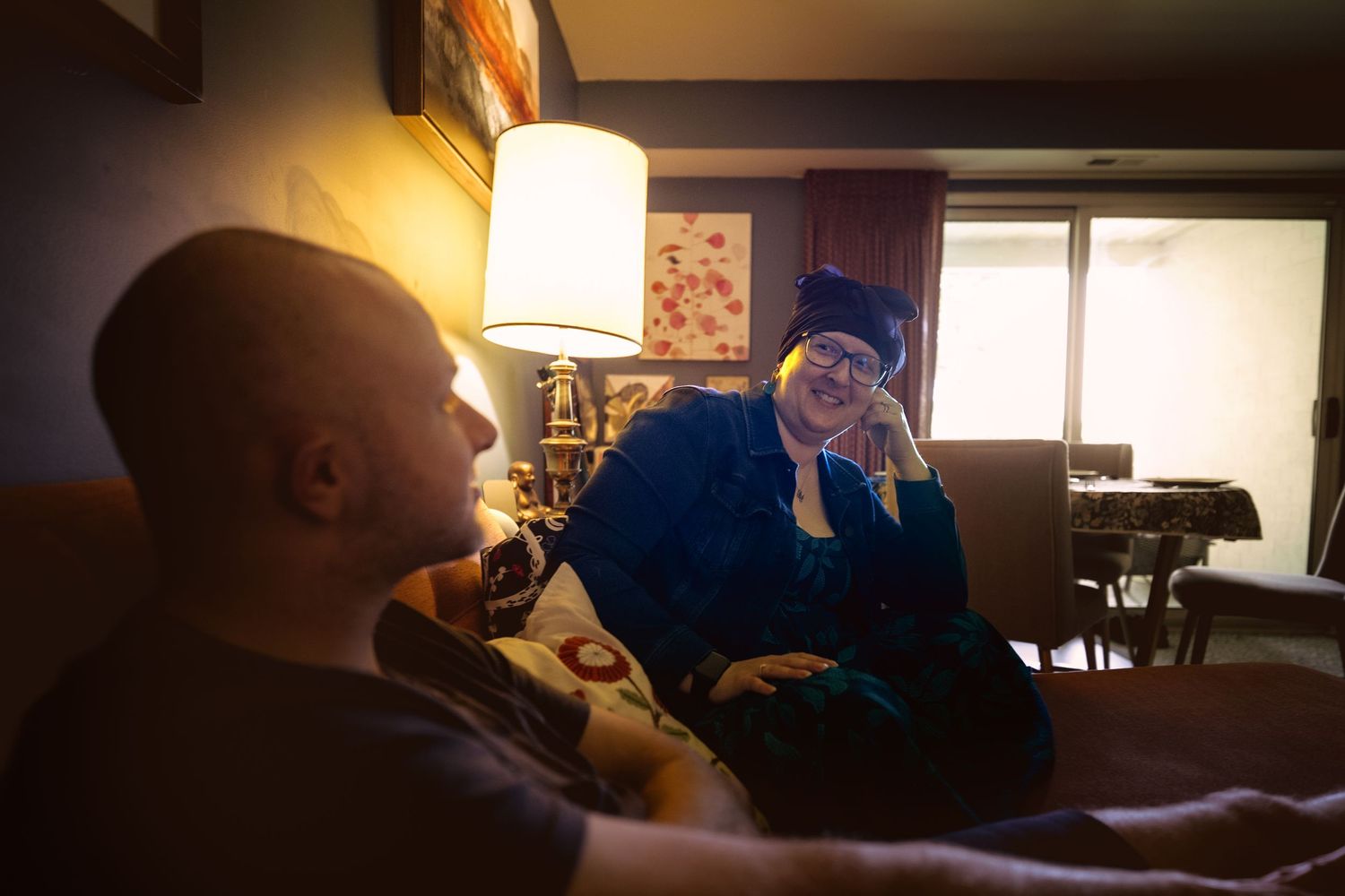 Two people relaxing indoors, one in graduation attire smiling warmly in a softly lit living room.