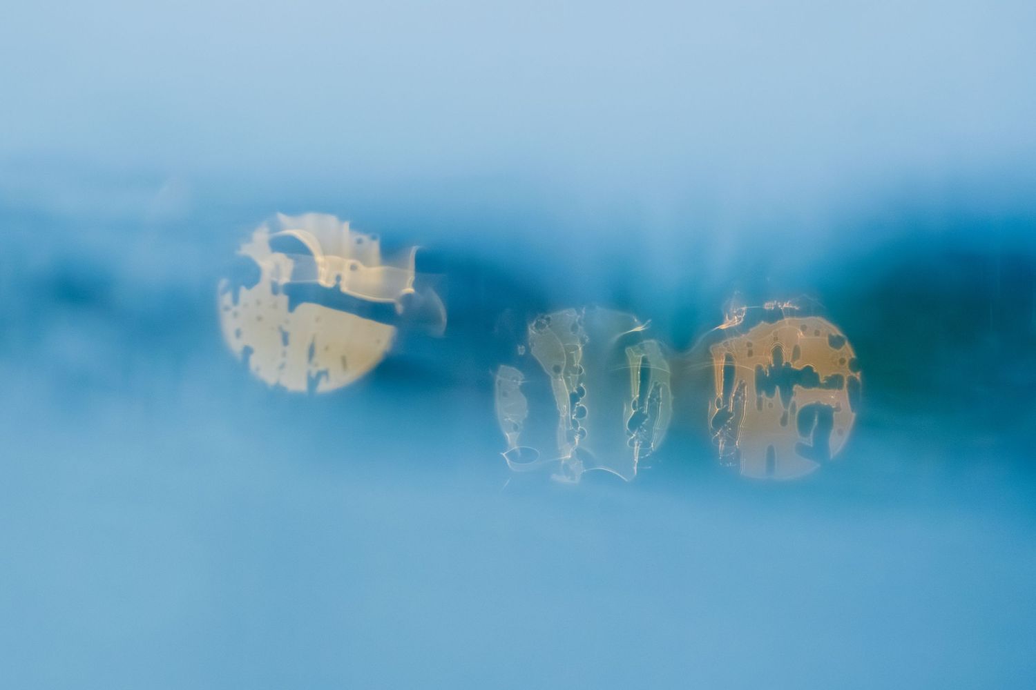 Abstract blue background with blurred reflections of buildings visible through water droplets on glass.