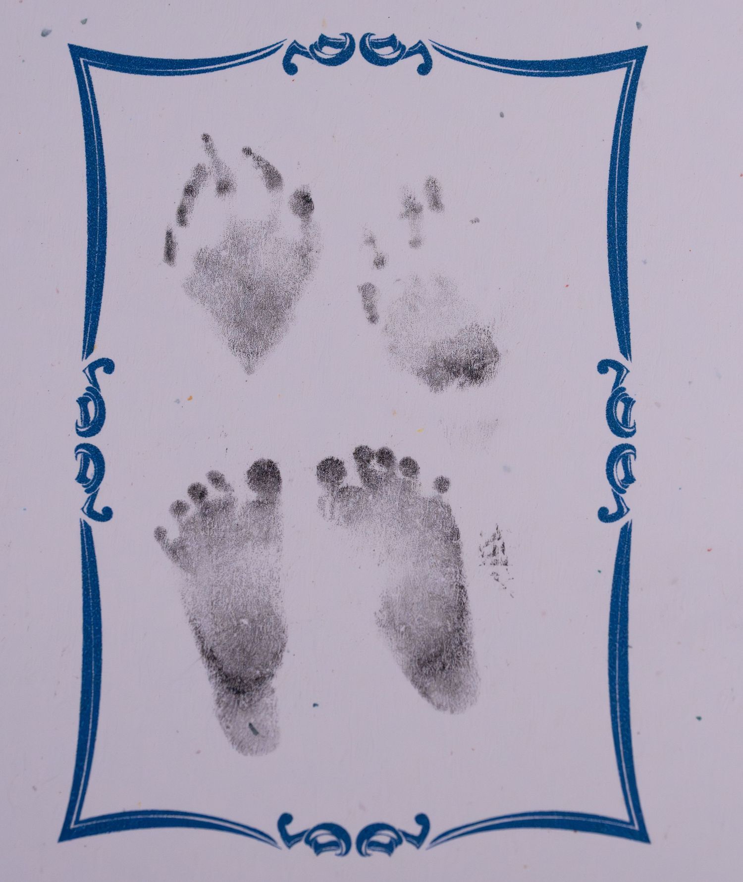 Baby hand and footprints in black ink displayed within a decorative blue border frame on light background.