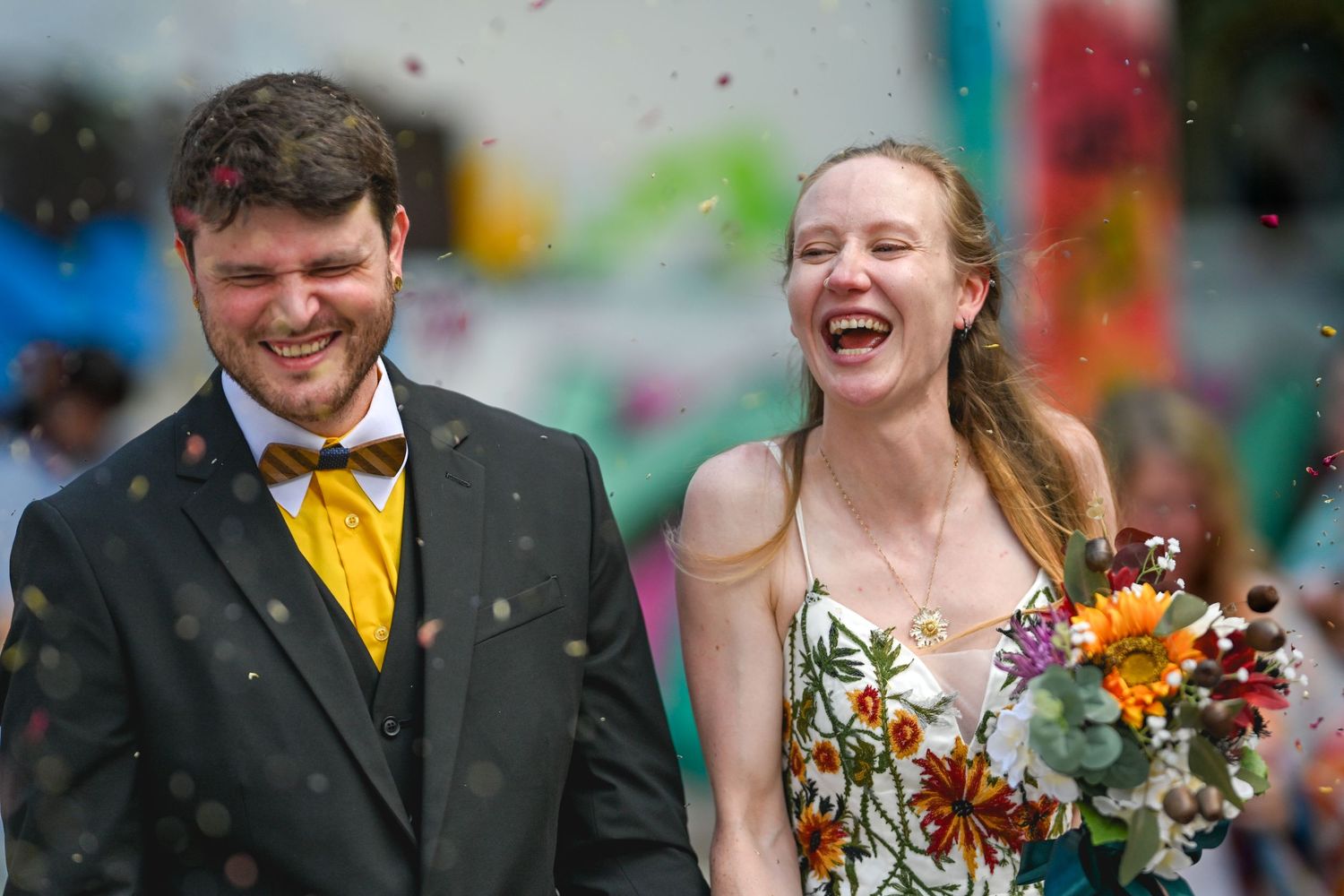 A wedding couple shares joyful laughter together while standing outdoors with vibrant autumn flowers in their decor.