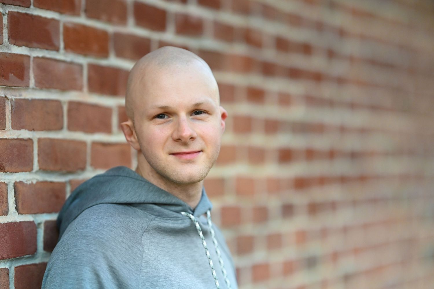 Athletic person in grey hoodie smiling against brick wall background.