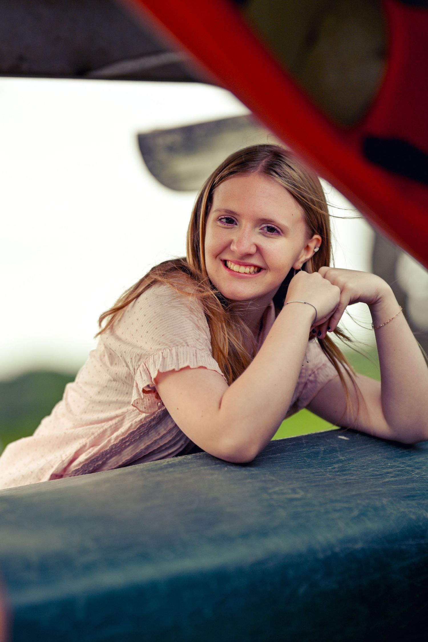 A person in a light colored blouse leans on a blue surface while posing at a park on a sunny day.