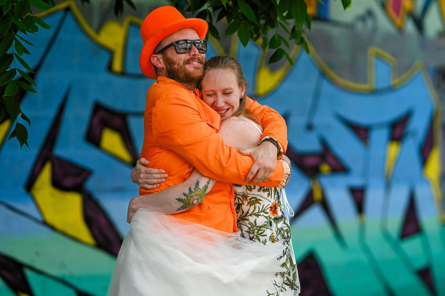 A tender embrace in front of a vibrant graffiti wall, both wearing orange in a heartwarming display of affection.