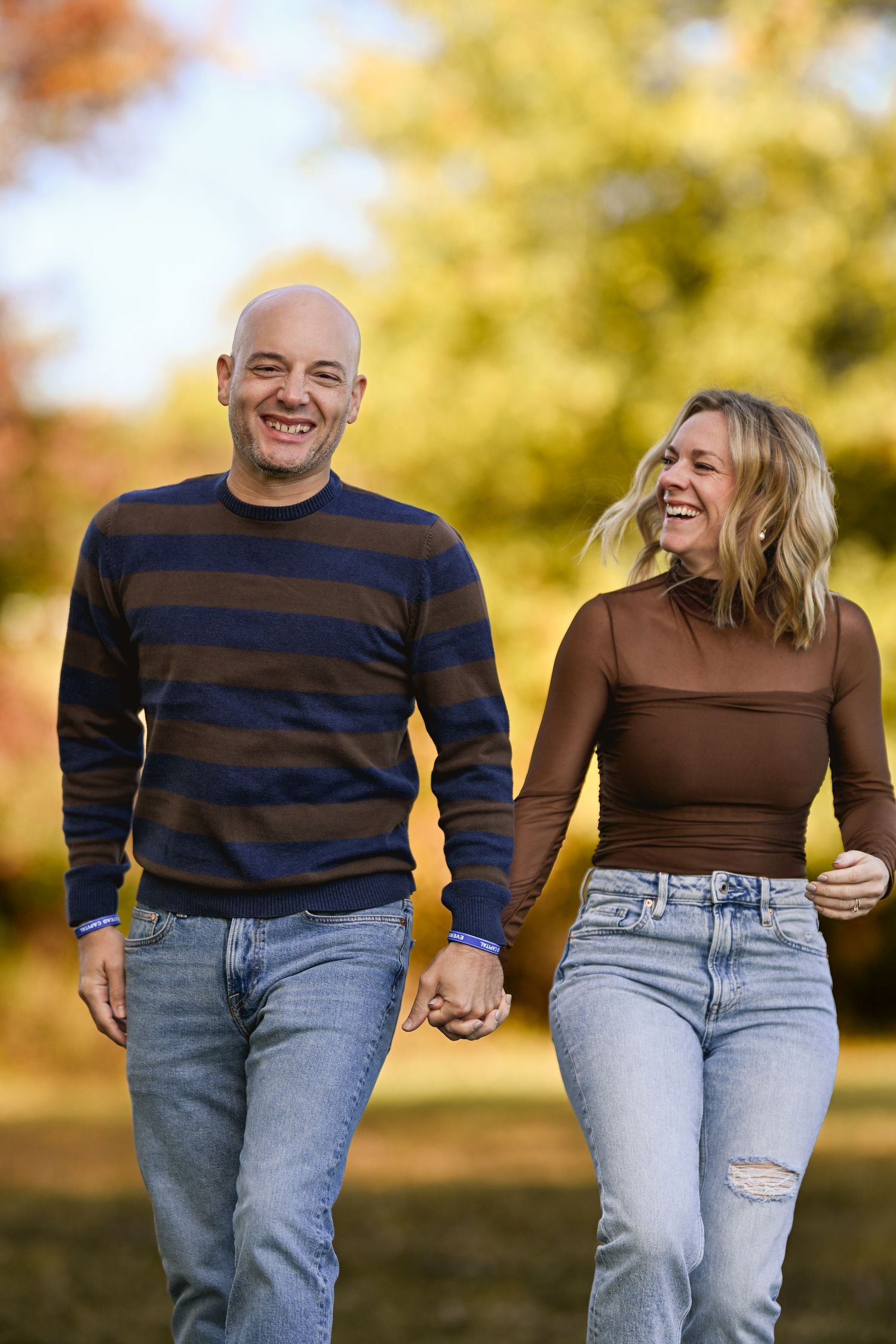 A couple wearing matching blue striped sweaters and jeans walks together in a park during autumn.