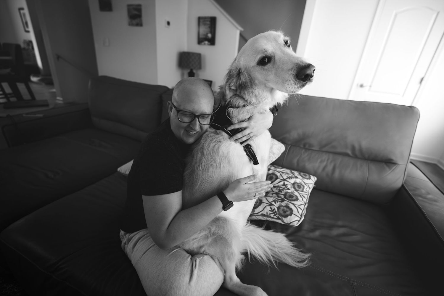 Man hugging a large white dog on a couch in a cozy living room, black and white photo.